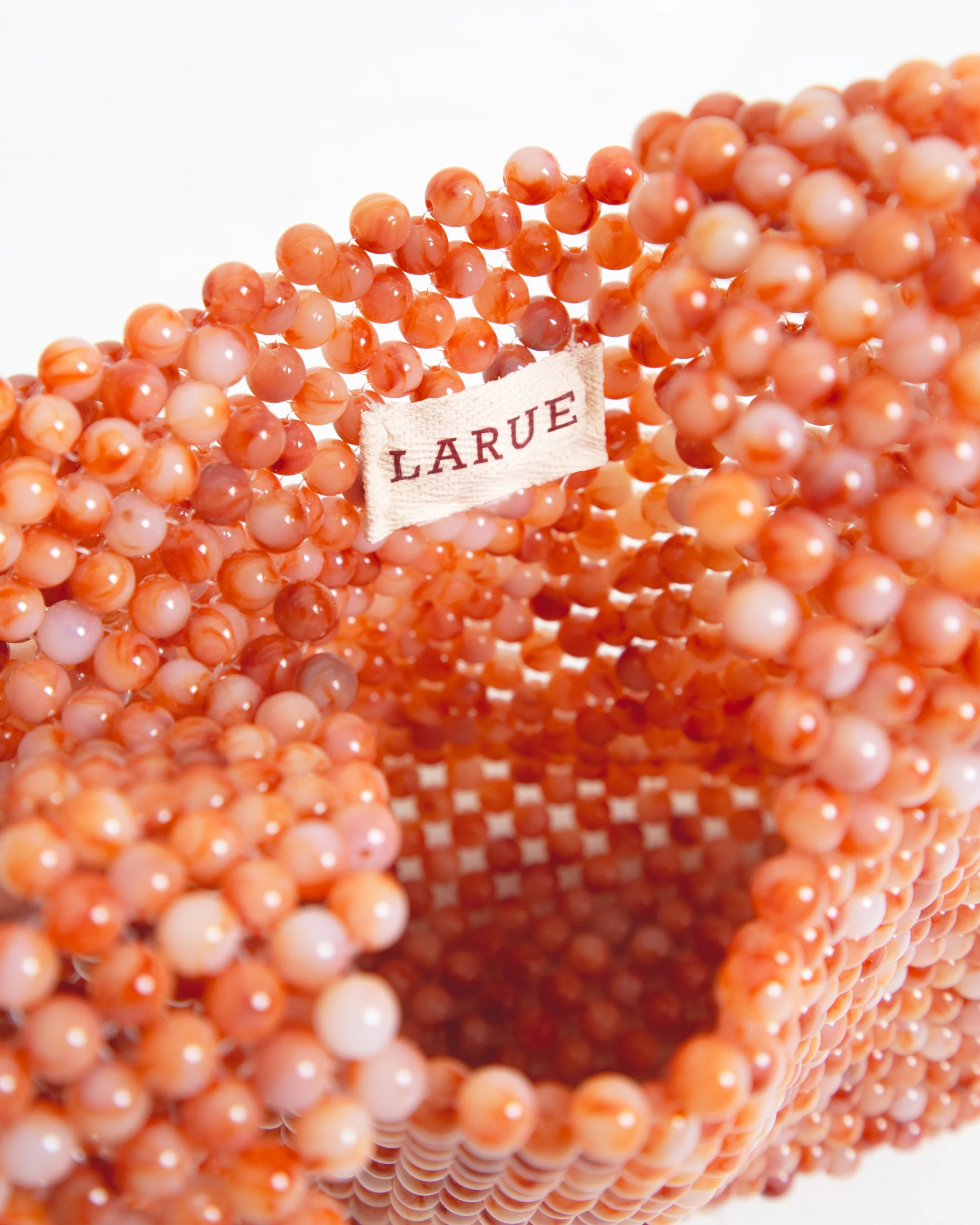 A peach-colored beaded necklace with a fabric tag reading 'LARUE' attached to it.