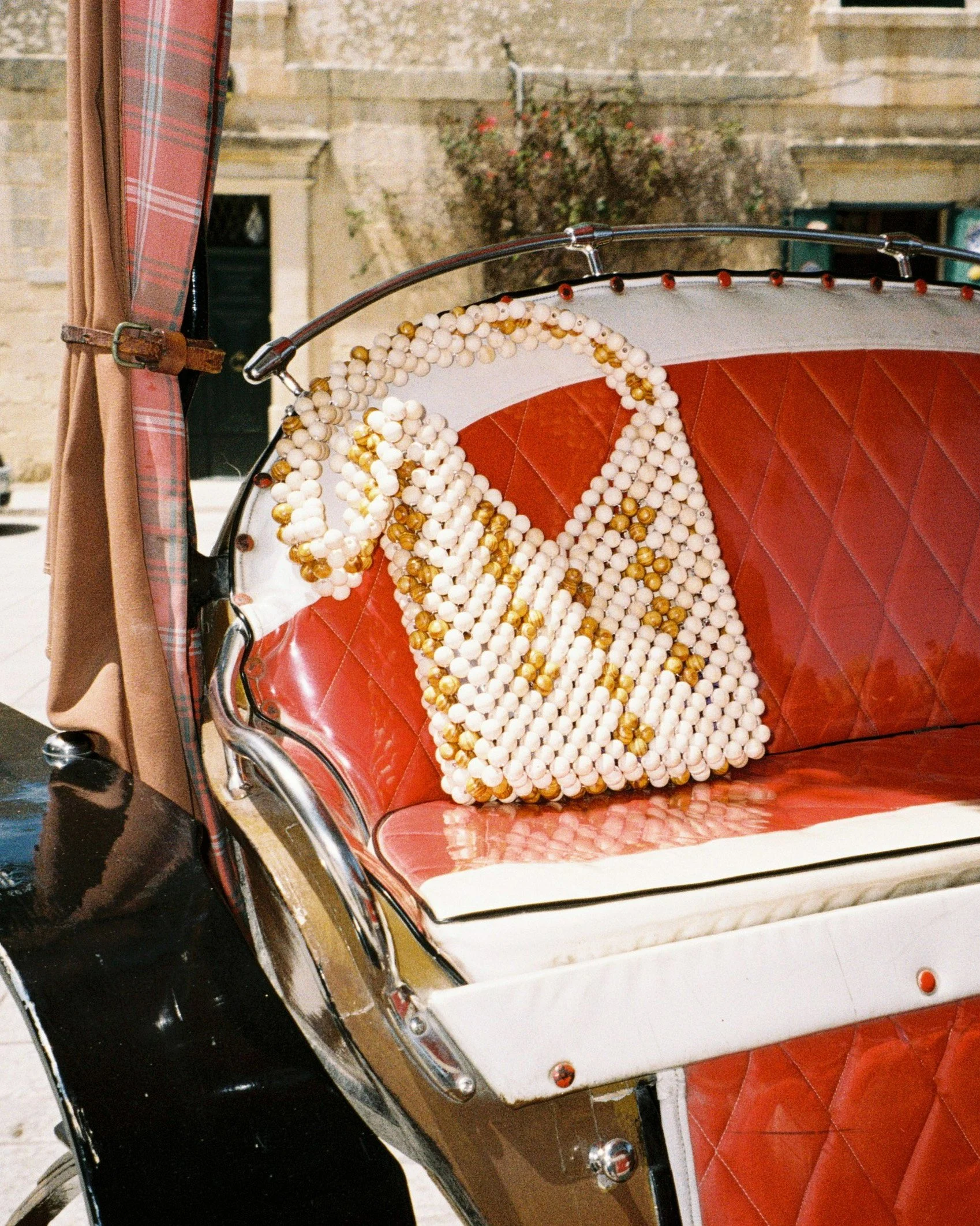A decorative bag made of white and gold beads with the word 'GRACE' written on it, placed on a red leather cushioned seat of a vehicle.