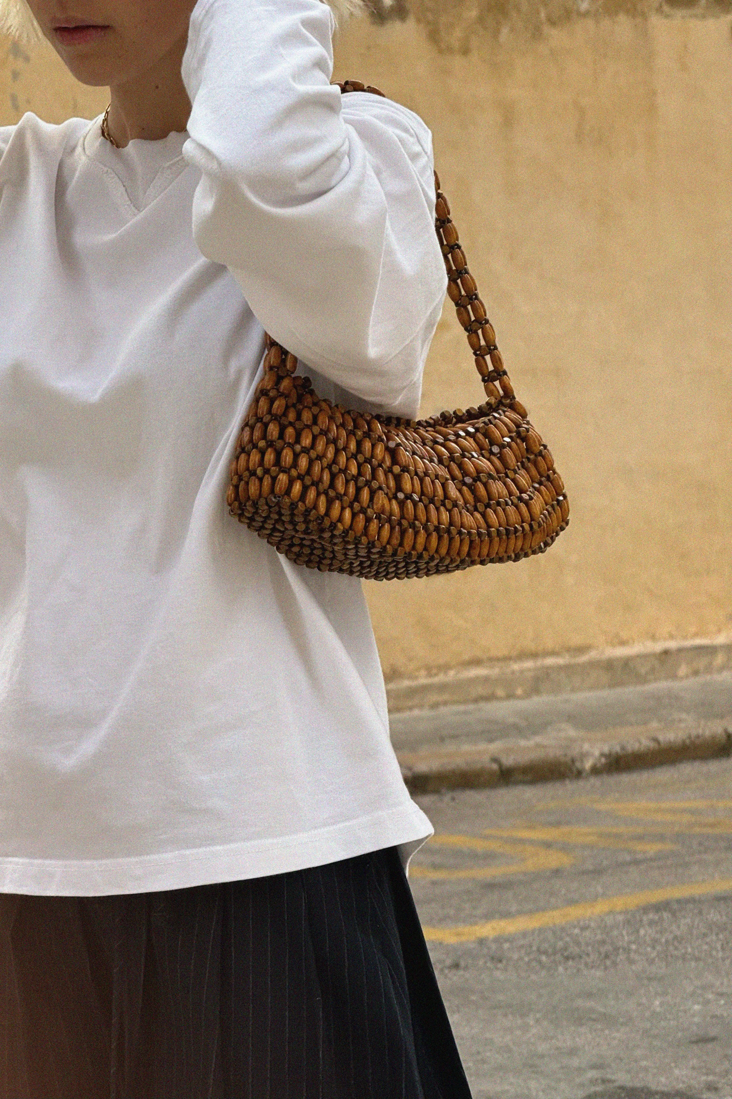 Person wearing a white long-sleeve shirt carrying a beaded brown handbag.