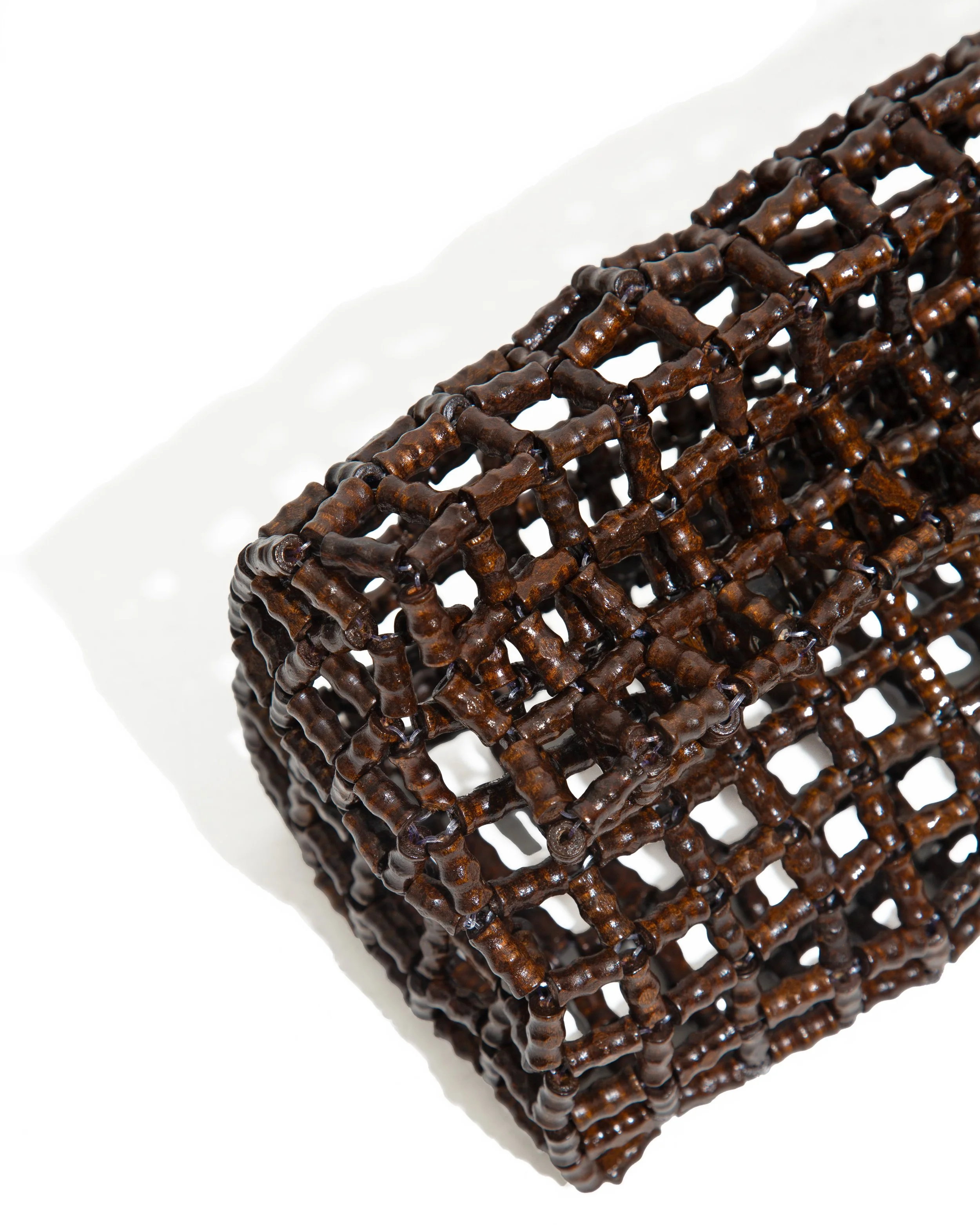 A close-up of a dark brown, open-set, cube-shaped woven or lattice structure casting a shadow on a white background.