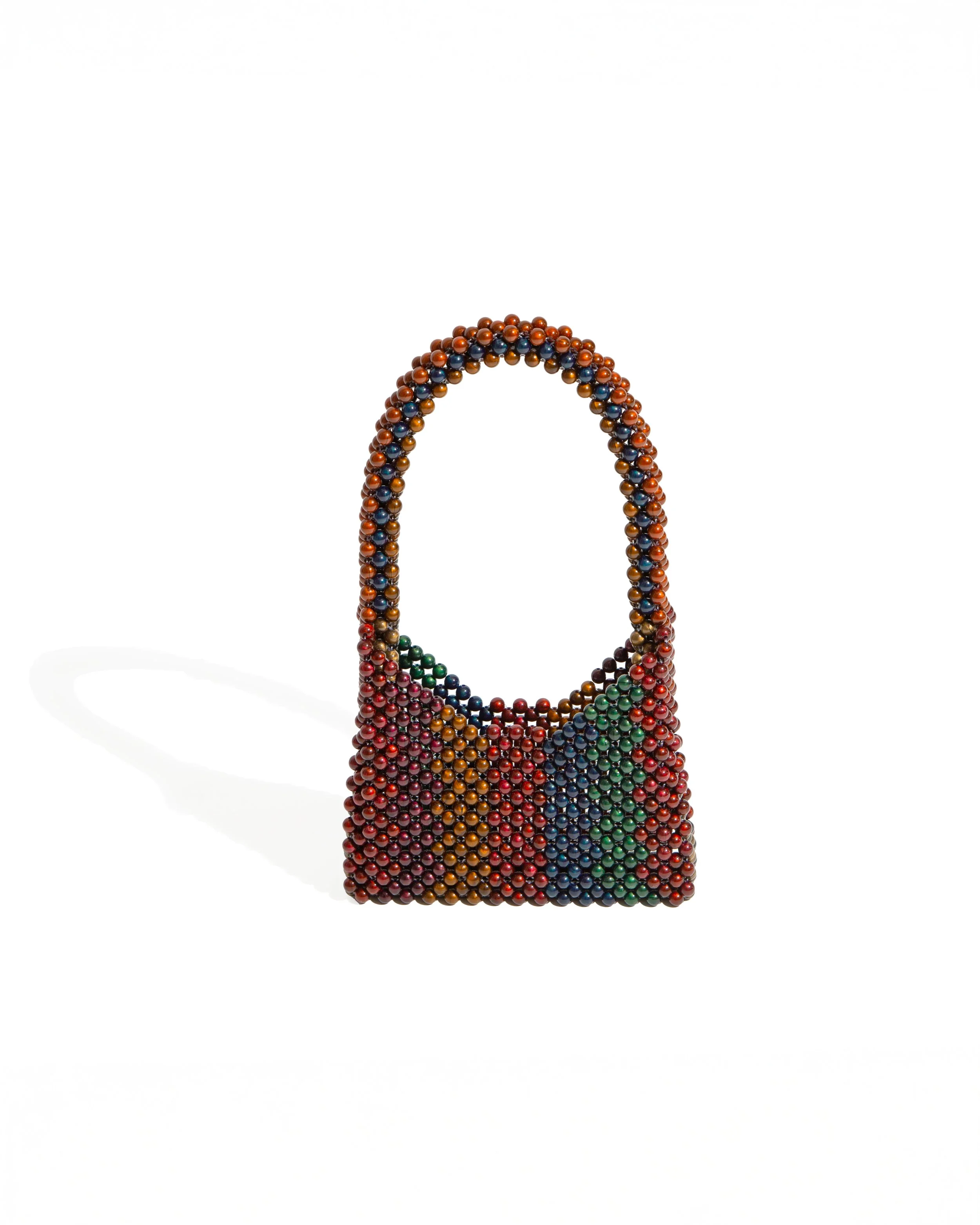 A handbag made of colorful miniature beads arranged in a patchwork pattern, casting a shadow on a white background.