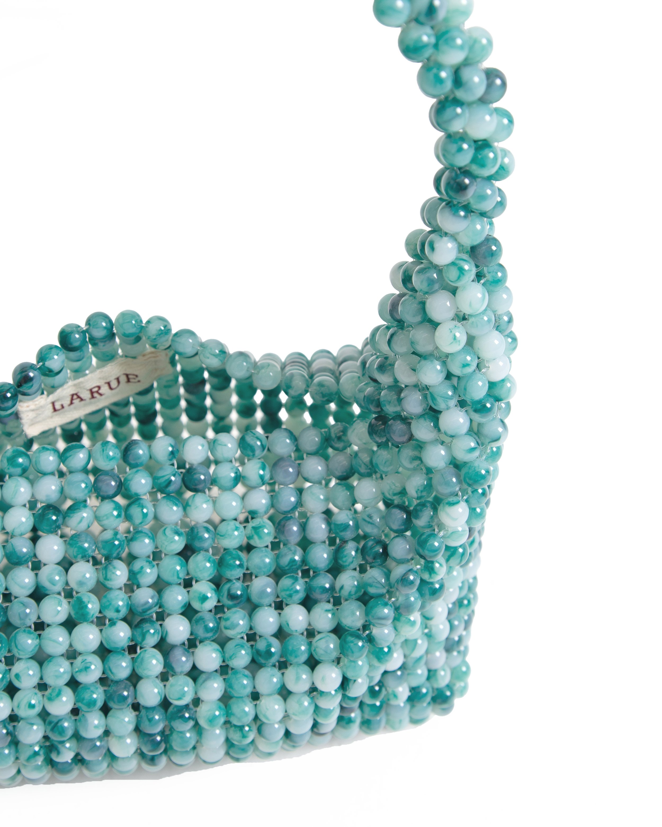 A handbag made of light blue and white pearls with a fabric label that reads "La Rue."