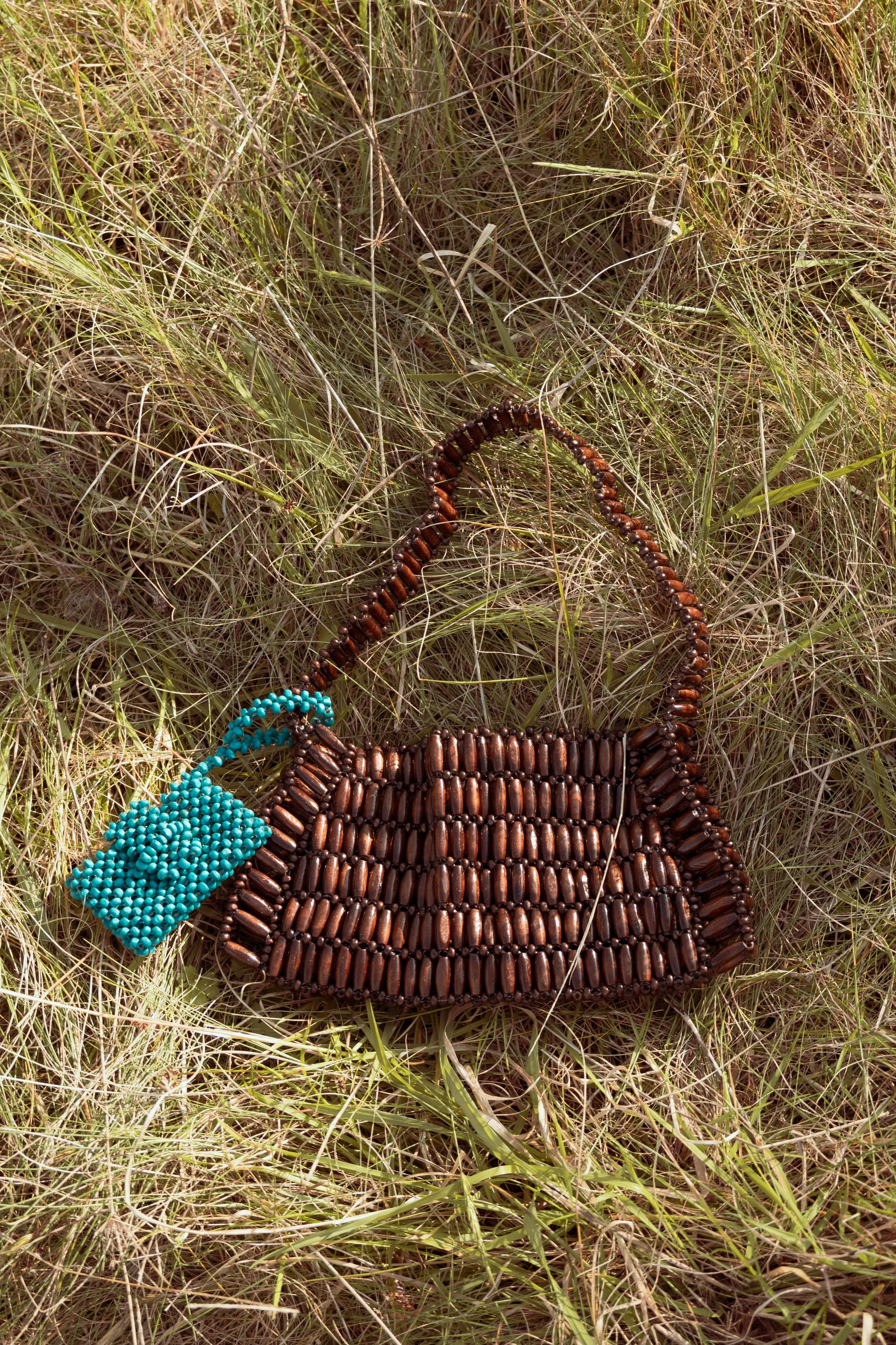 Handmade beaded handbag with brown beads and a turquoise beaded accessory, lying on grass.