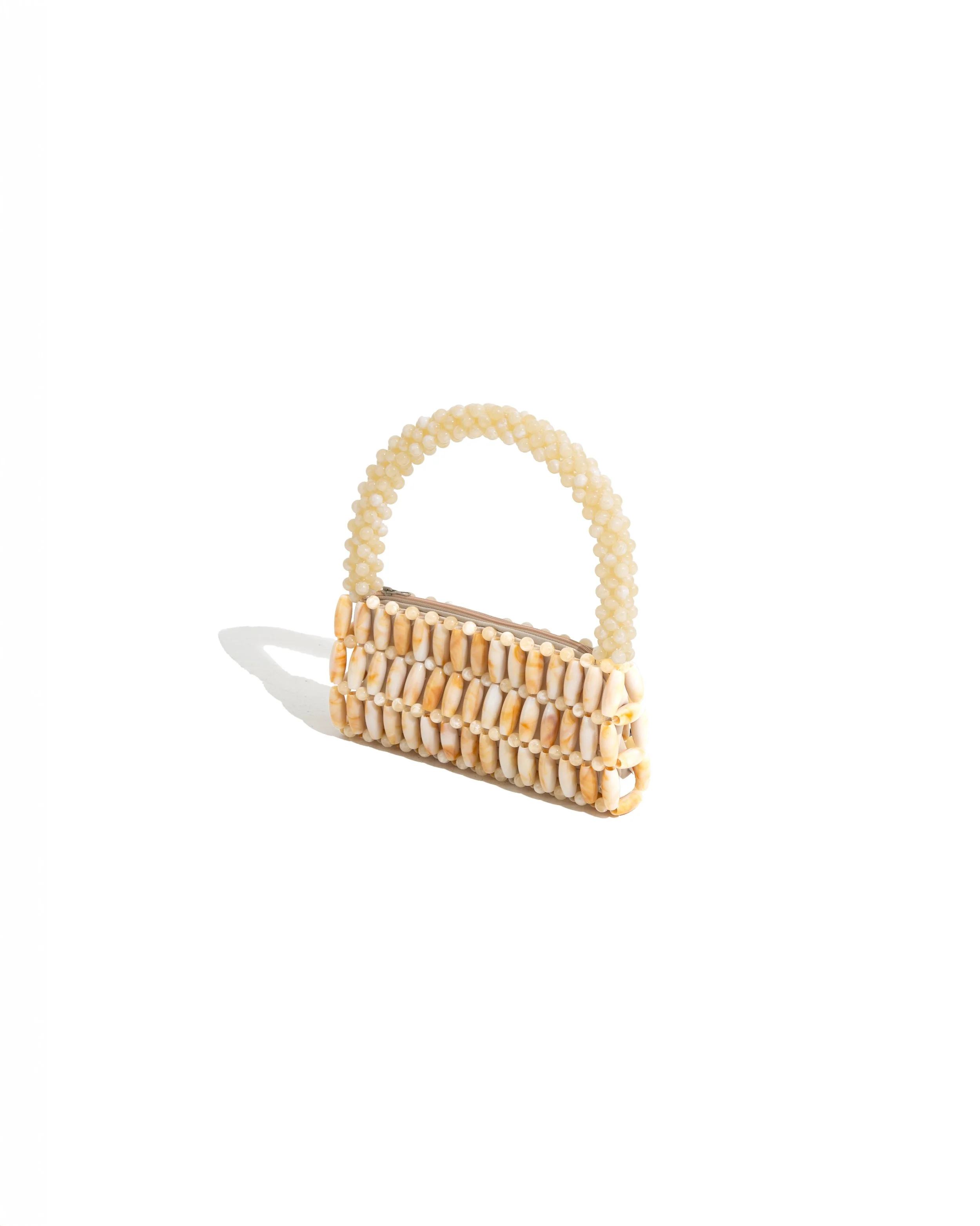 A handbag made of small beige shells and beads, with a beaded handle, on a white background.