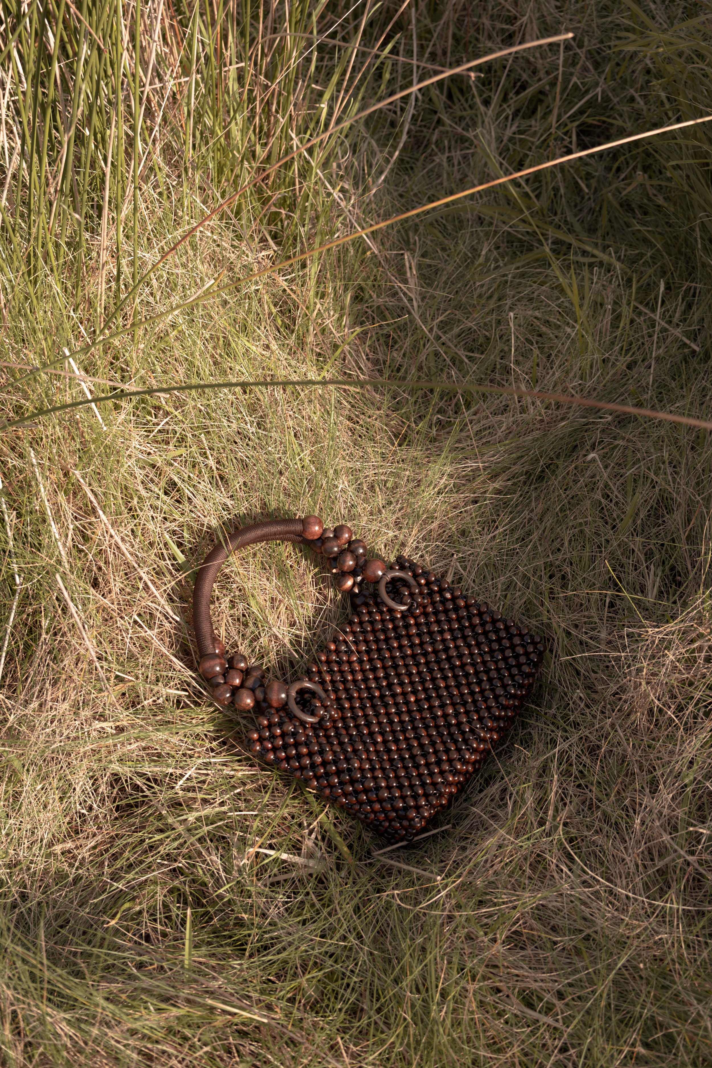 A brown beaded handbag with a rounded handle lies on grass.