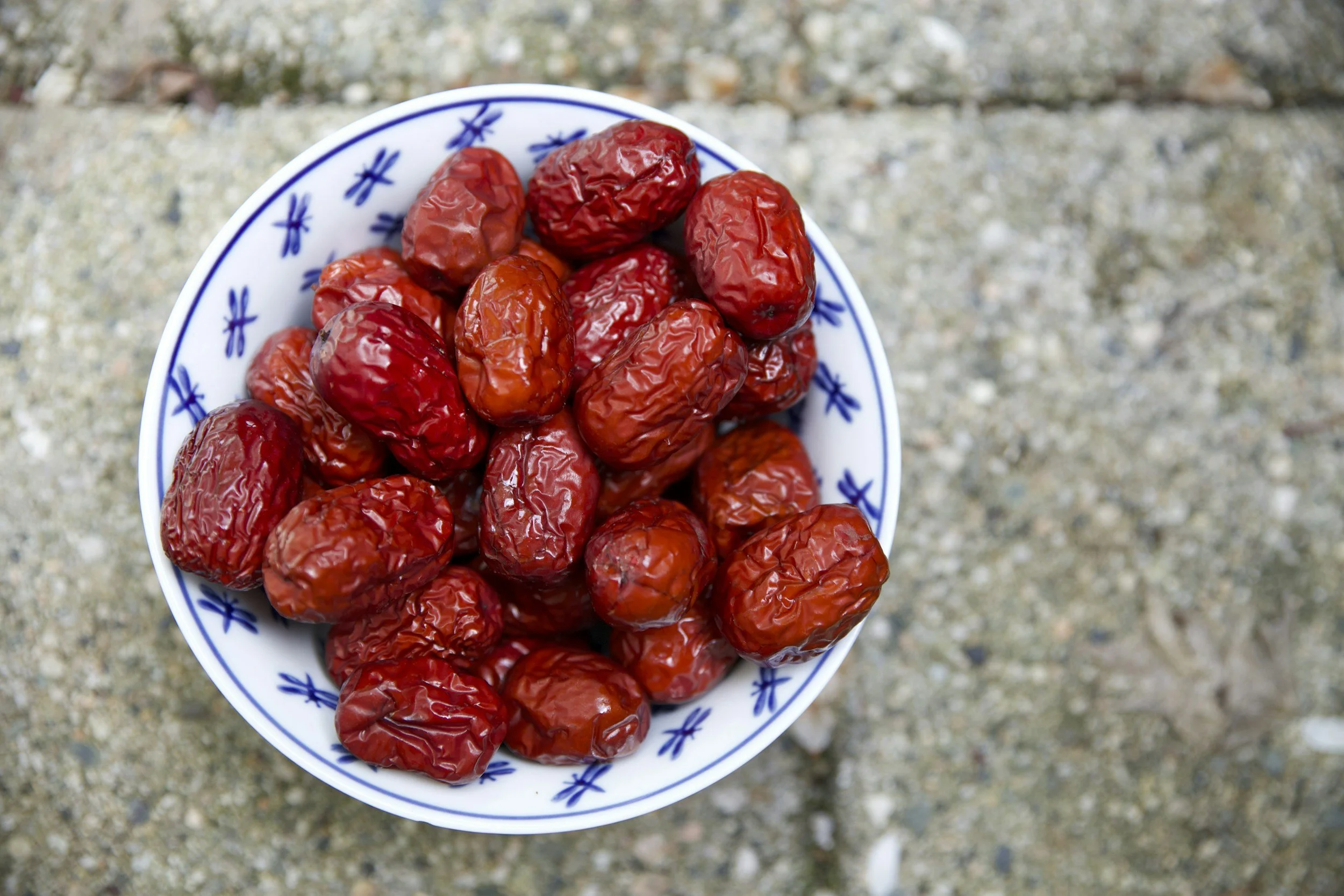 A bowl filled with dried red dates placed on a textured outdoor surface.