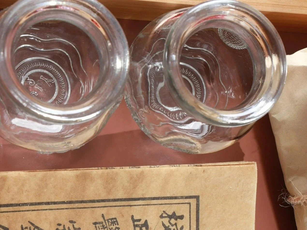 Two clear glass jars viewed from above, placed on top of a piece of paper or book with Chinese characters.