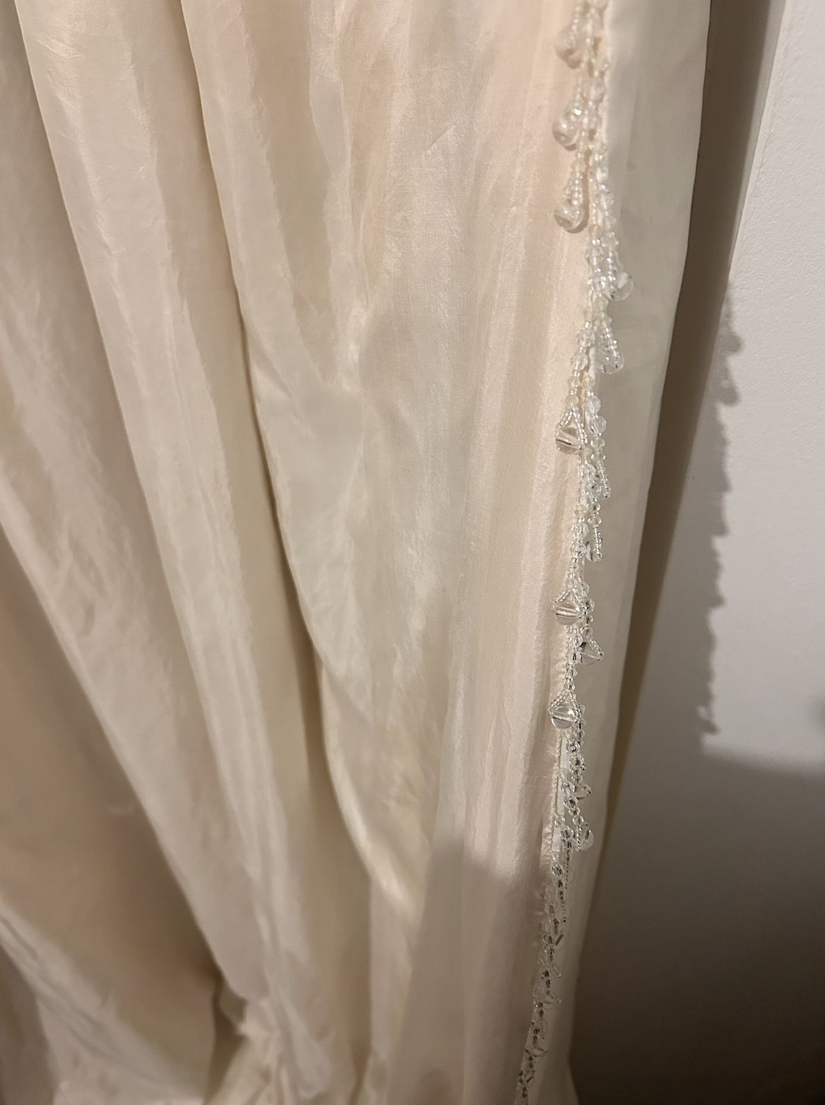 Close-up of a beige or cream-colored curtain with ornate bead and lace trim along the edge.