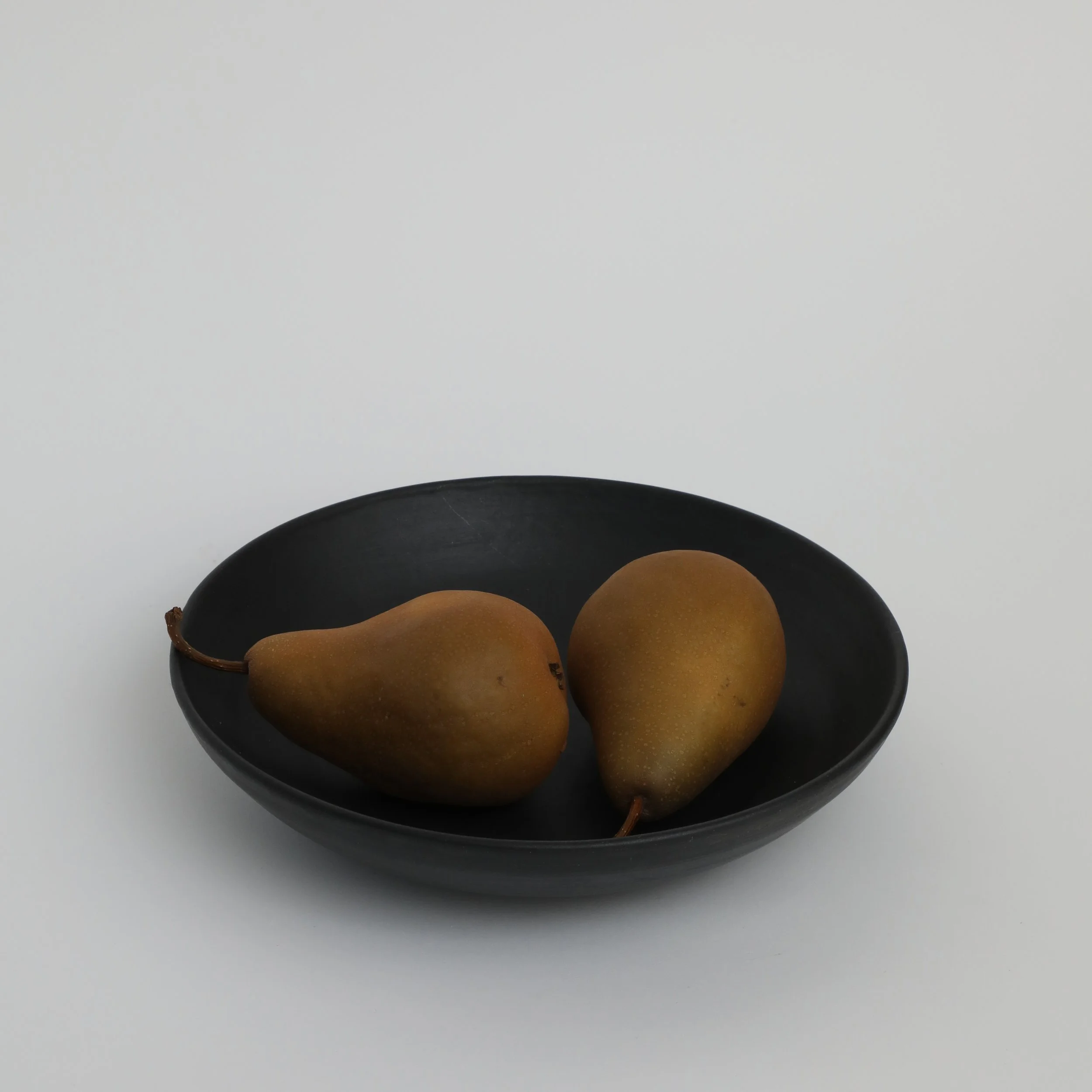 A black bowl with pears, placed on a white surface with a plain white background.