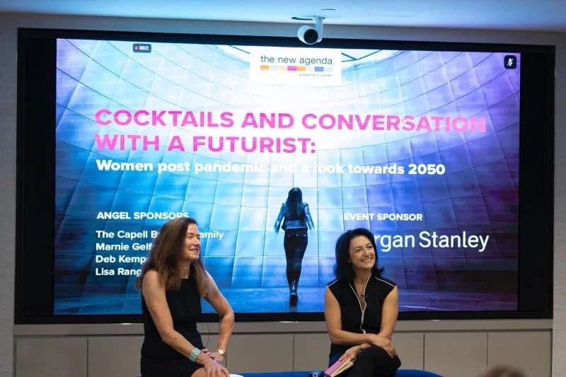 Panel discussion at a conference with a large screen displaying the title 'Cocktails and Conversation with a Futurist: Women post pandemic and a look towards 2050' and sponsor logos, featuring two women sitting and smiling on stage.