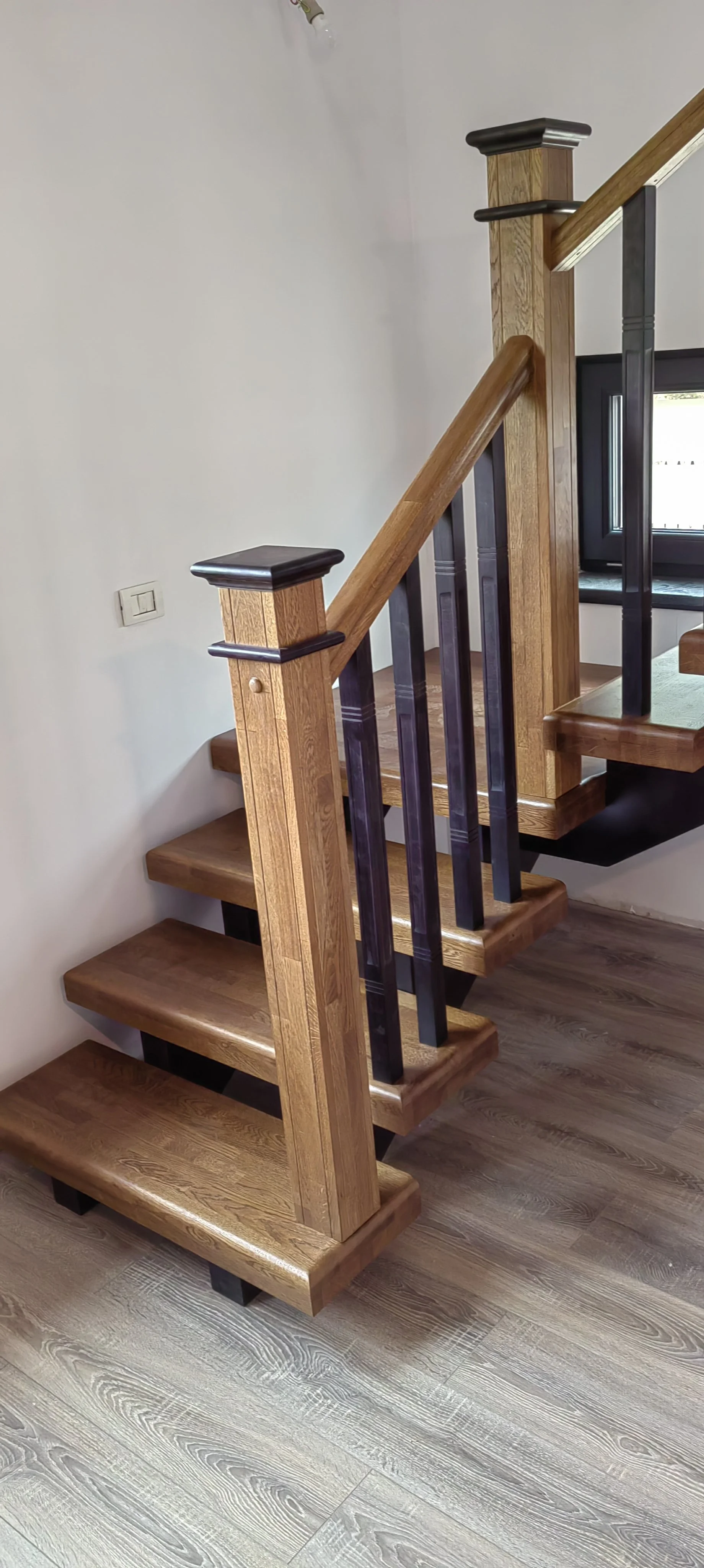 Wood staircase with black metal railings and natural wood finish, sitting against a white wall near a window.