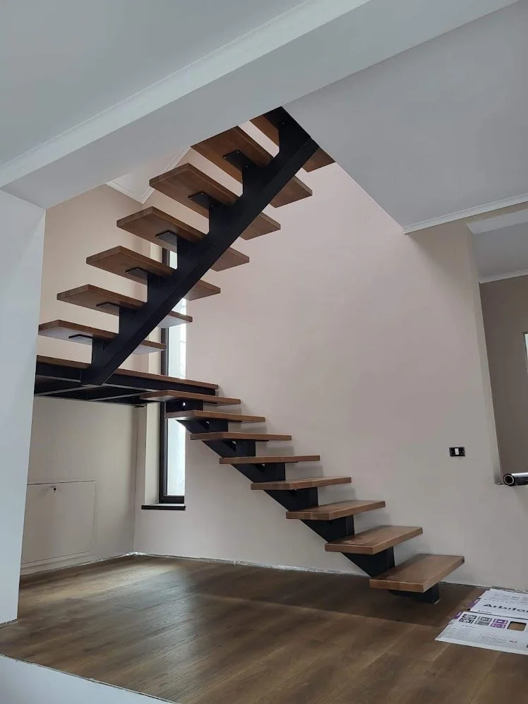 Interior view of a modern floating staircase with wooden steps and black support structure in a room with hardwood flooring and minimal decor.
