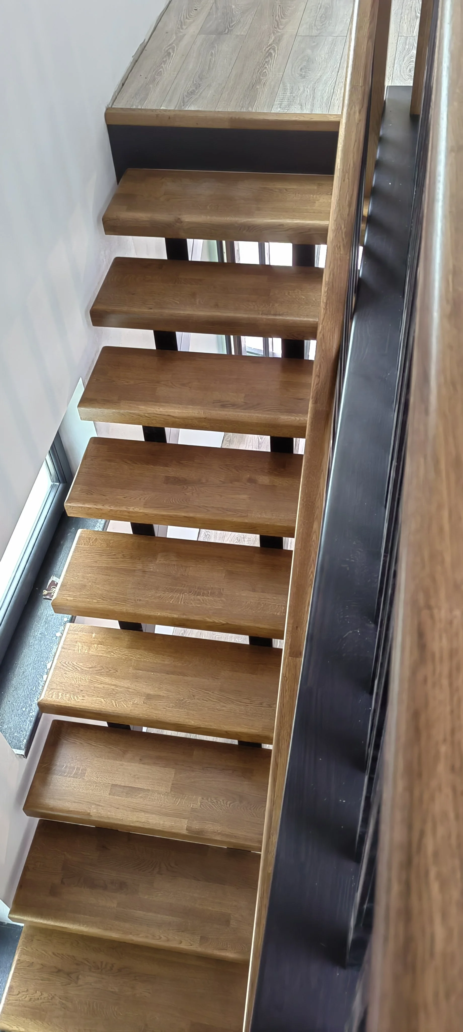 Close-up of wooden staircase with black stringer, viewed from below, showing the alternating steps.