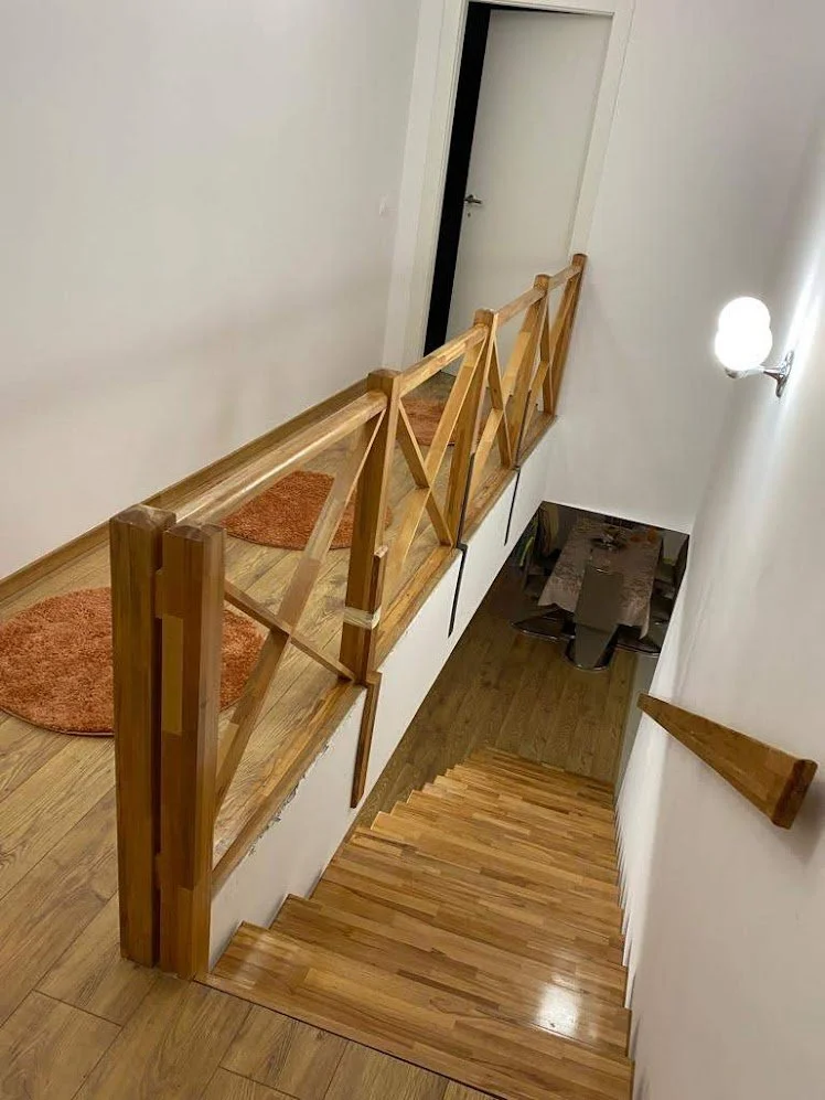 Wooden staircase leading down to a dining area, with a white wall, a wall-mounted light, and orange mats on the landing.