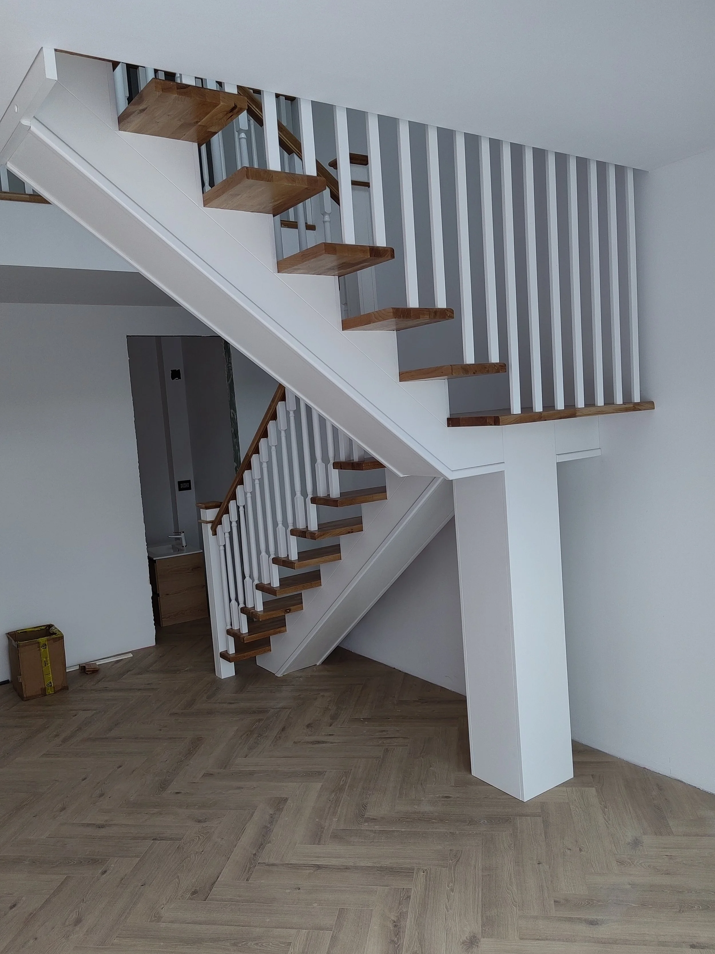 Empty staircase with wooden steps and white railings leading to an upper floor in a modern house, with wood-patterned flooring.