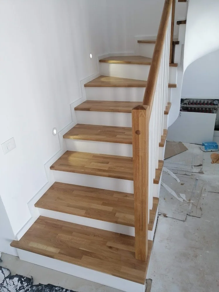 Wooden staircase with white risers and handrail, under construction in a residential space.