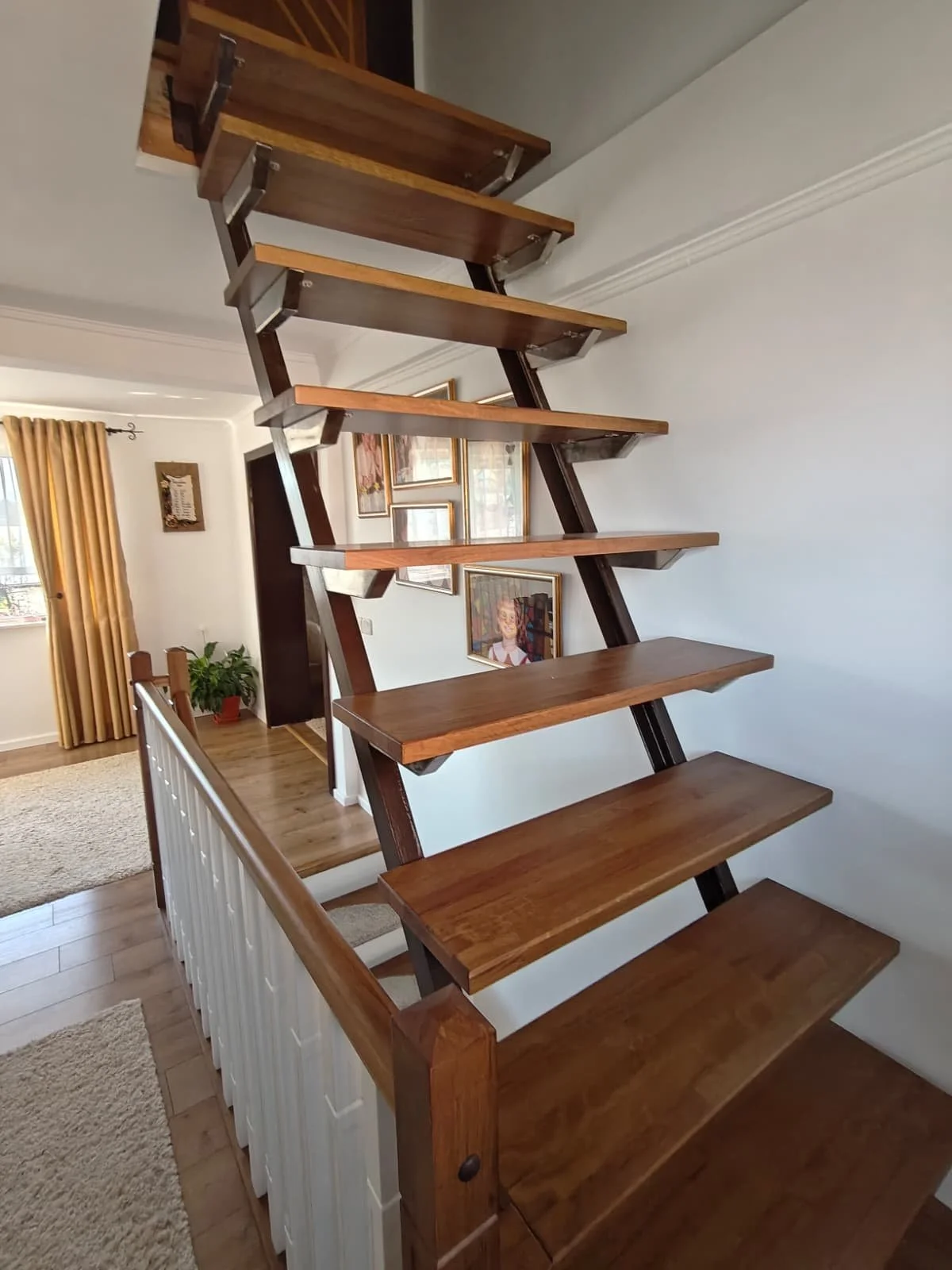 Wooden staircase with open risers next to a picture wall in a home interior.