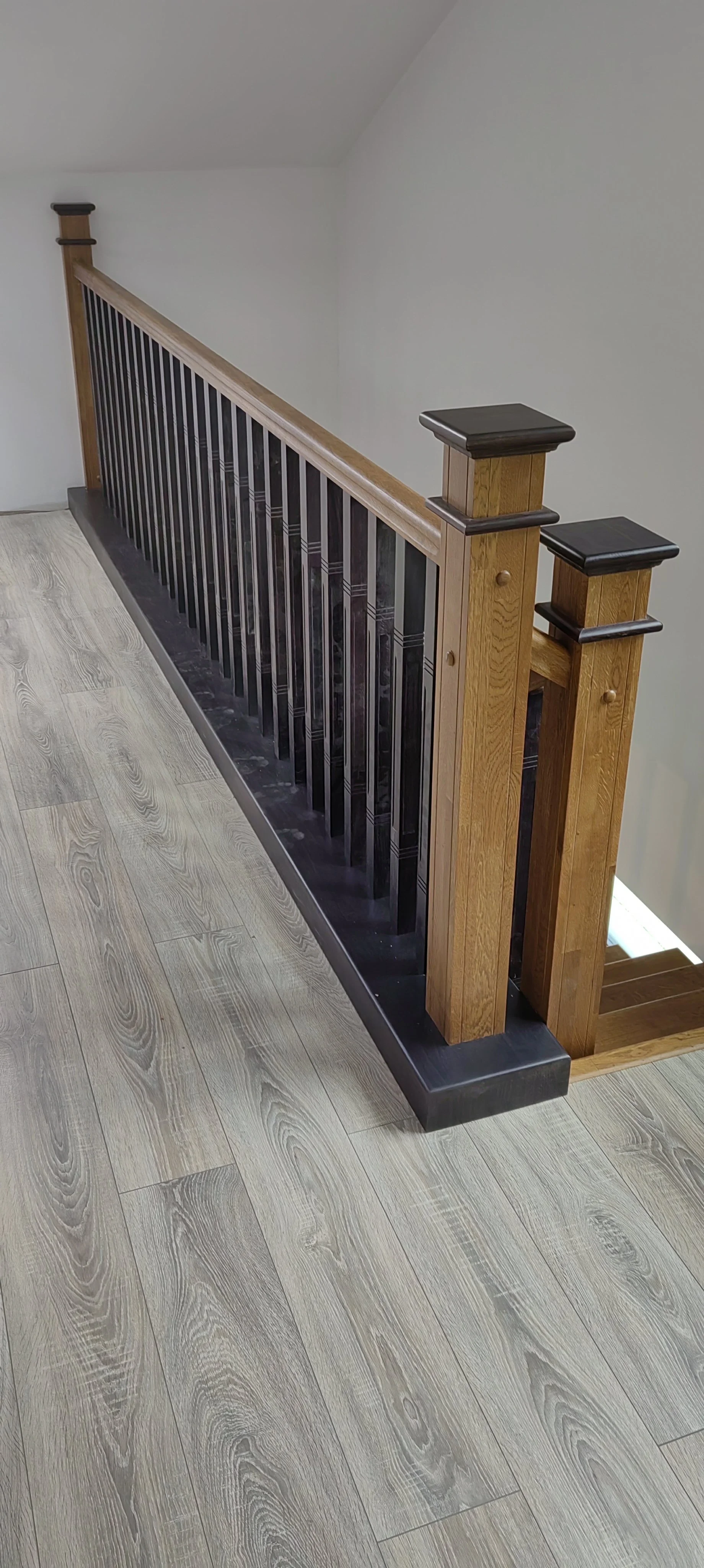 Wooden stair railing with black metal balusters and light wood flooring.