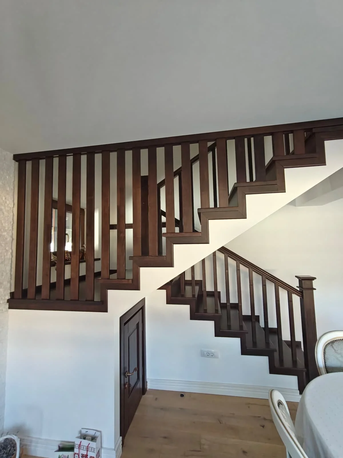 Interior view of a wooden staircase with dark wood railings and white walls.