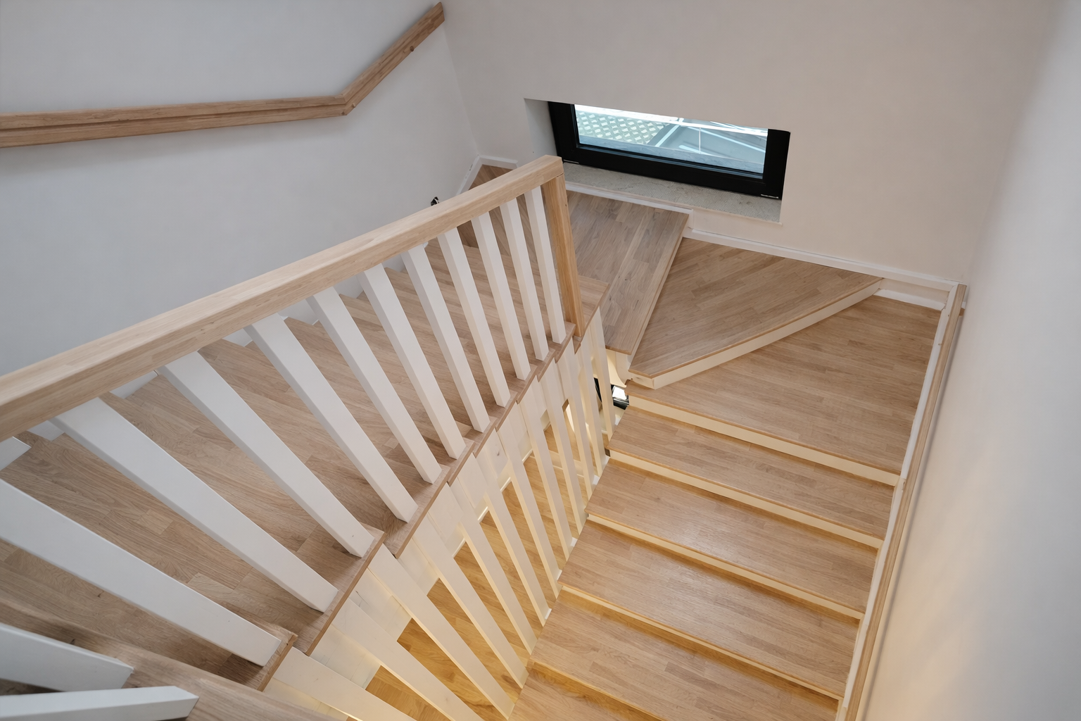 Wooden staircase with white balusters and a black window at the bottom.