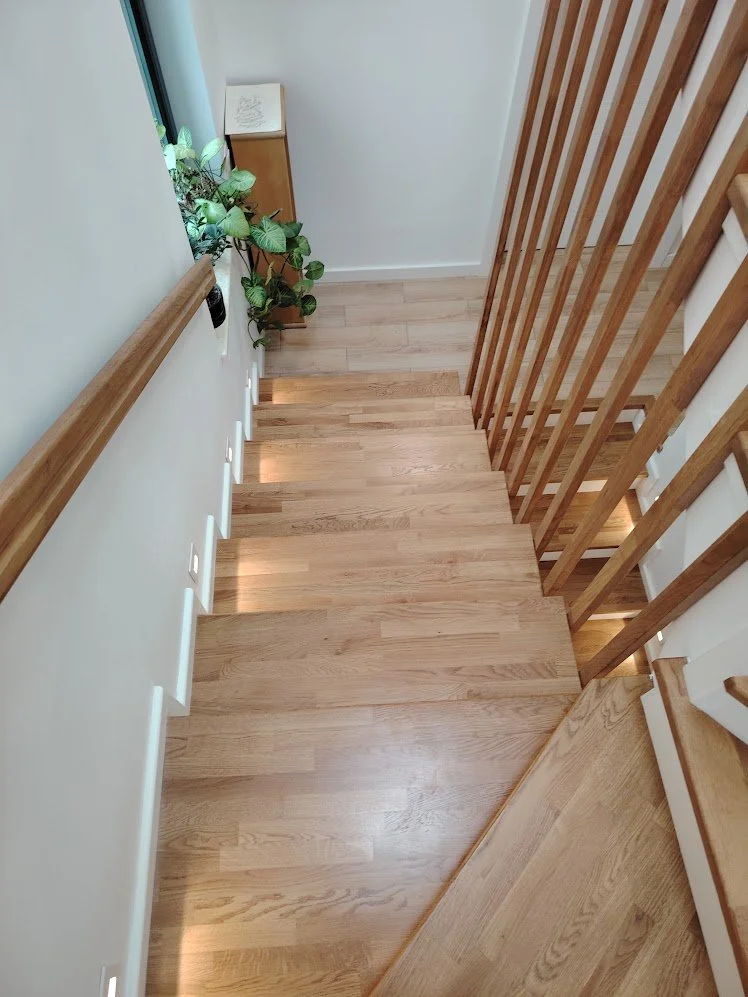 Wooden staircase with built-in lighting along the edge of each step, white walls, a small green potted plant near a window, and a small cabinet with a decorative item on top.