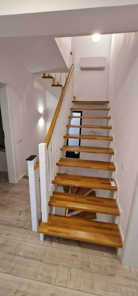 Wooden staircase with a white railing and gold handrail leading upstairs in a modern home with white walls and light-colored flooring.