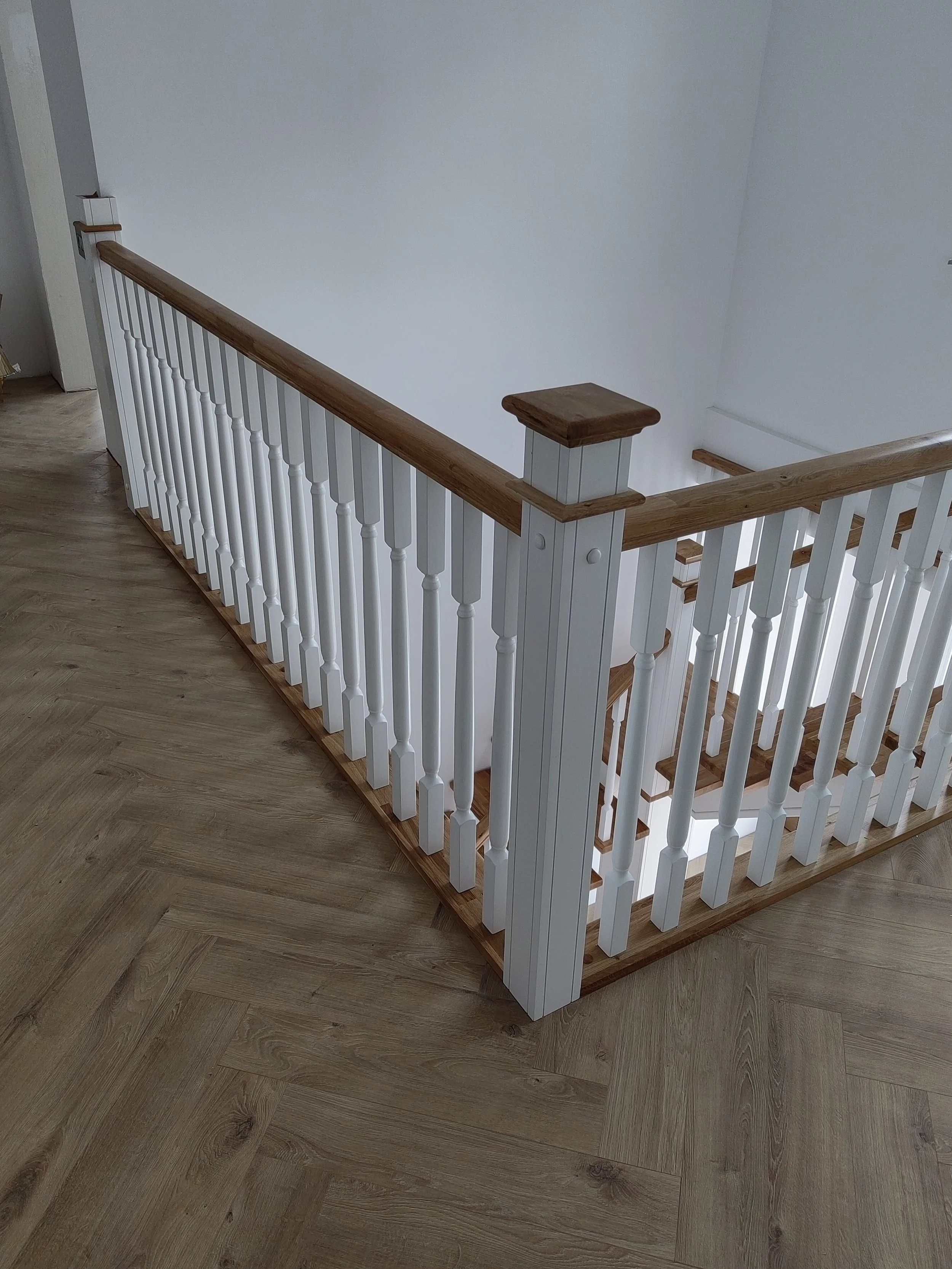 Wooden staircase with white balusters and a wooden handrail, viewed from the top.