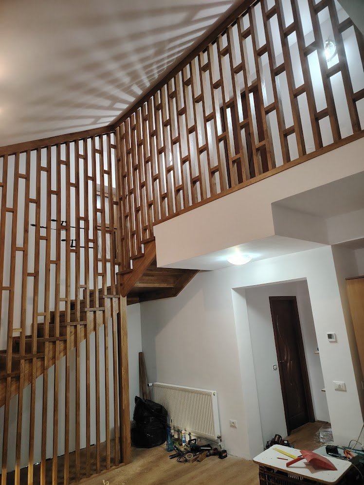 Interior view of a staircase with a wooden railing in a modern home, with some construction tools and materials visible on the floor.