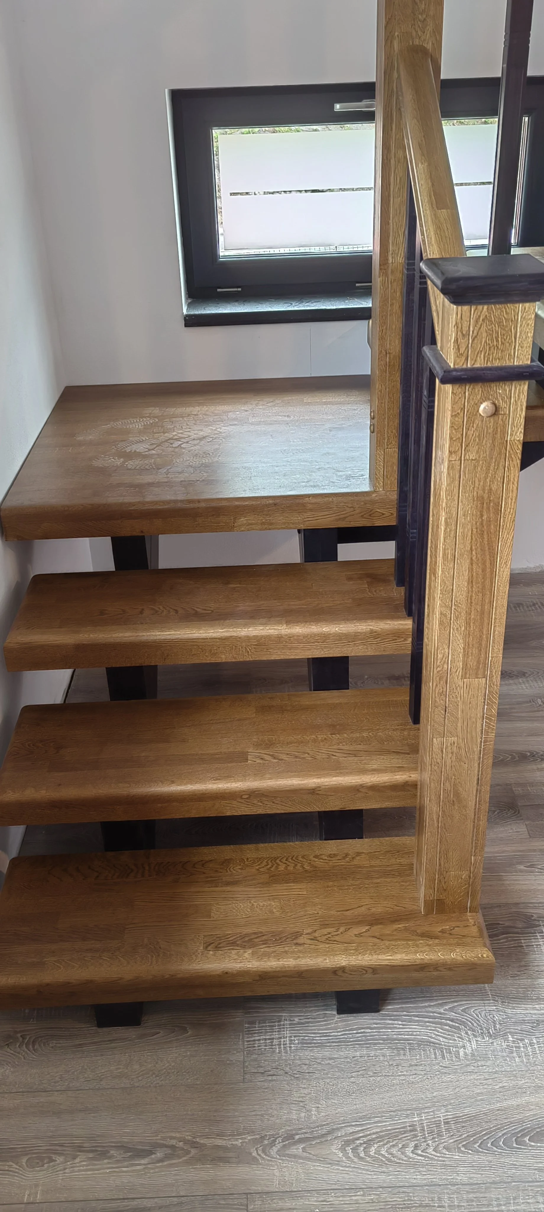 Wooden staircase with open risers and black metal supports, next to a window.
