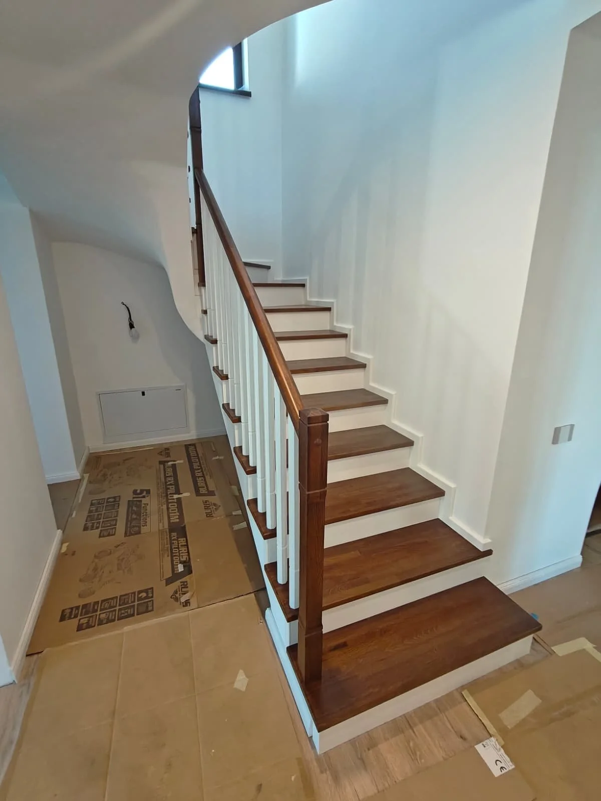 Interior view of a staircase with wooden steps, white risers, and a wooden handrail, in a partially finished house.