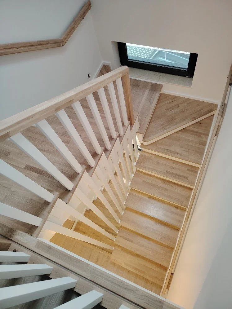 View looking down a staircase with light wood steps, white balusters, and a black window near the bottom of the staircase.