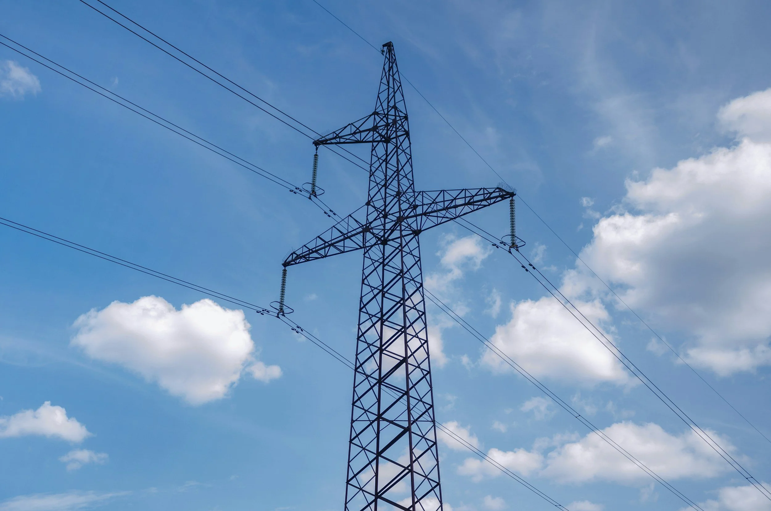 A black metal electrical transmission tower against a blue sky with scattered white clouds.