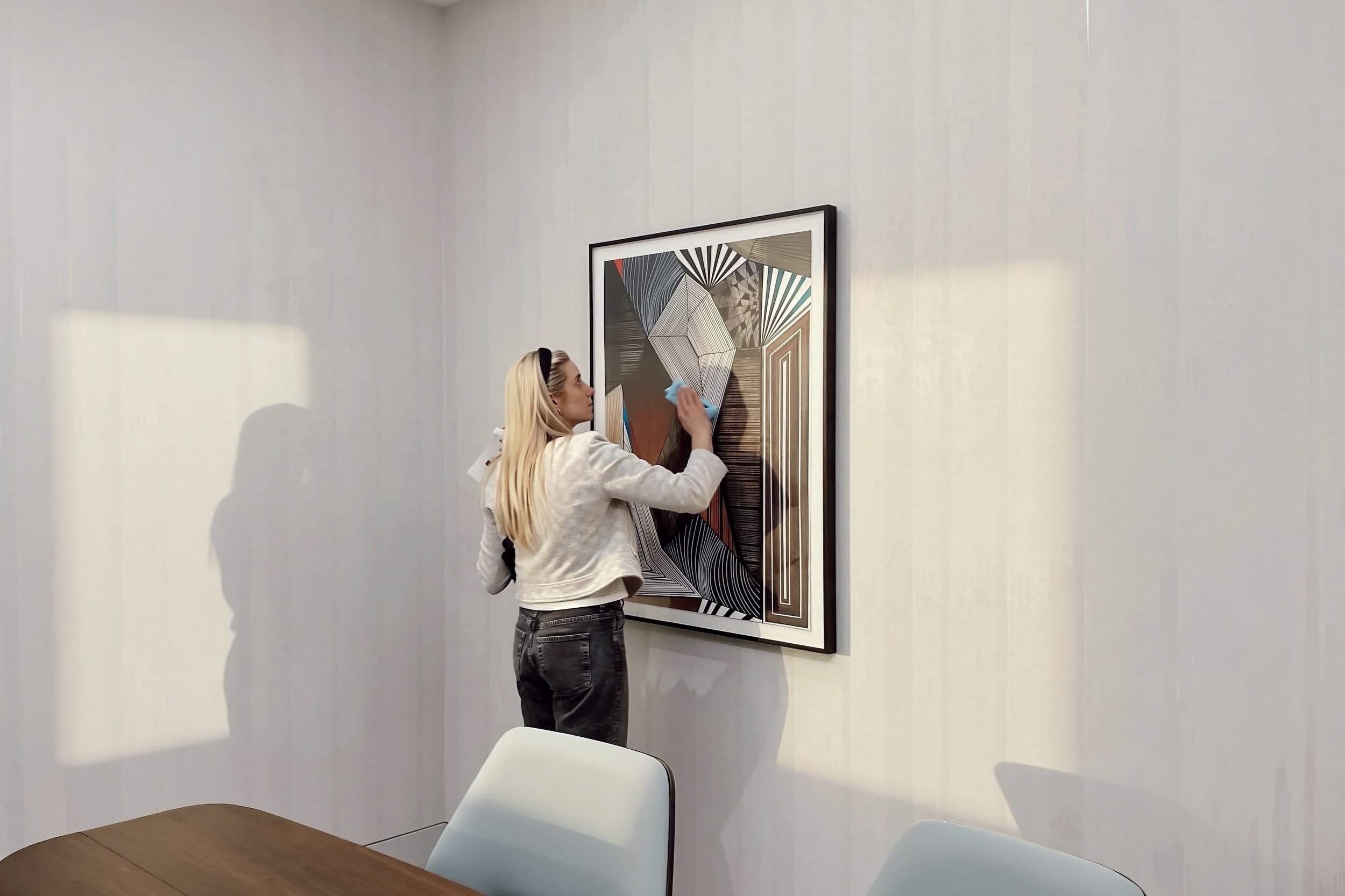 DeGroot Fine Art consultant carefully cleaning a framed artwork after installation in a corporate setting as part of ongoing maintenance and care services.