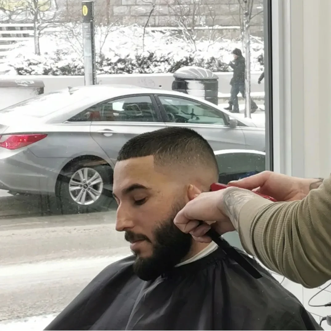 A man getting a fade haircut in a barbershop with snow outside the window.