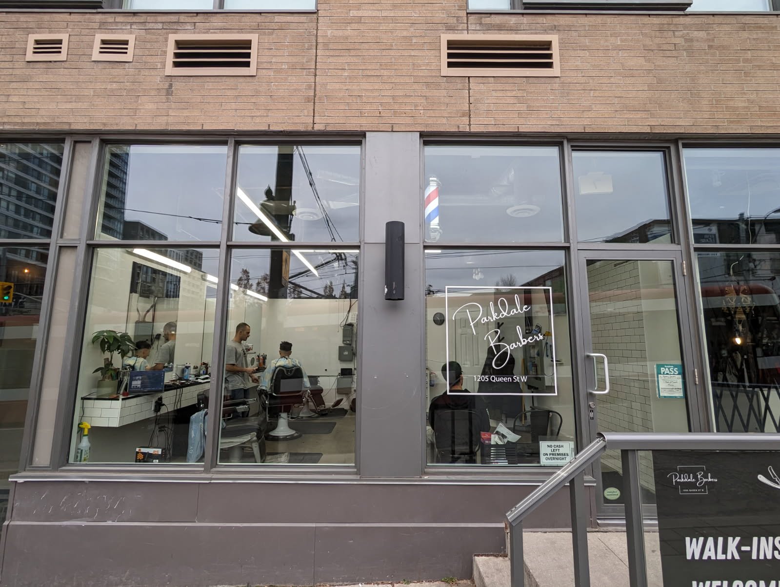 Outside view of a barbershop with glass windows, sign reading 'Parkdale Barbers,' and people getting haircuts inside.