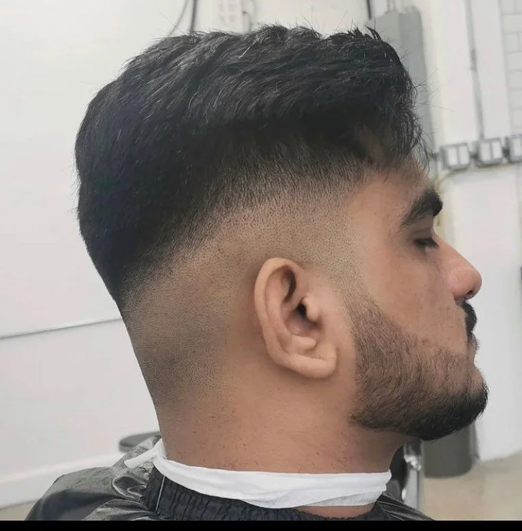 Side view of a man at a barber shop with a fresh hairstyle featuring a fade haircut and short beard.