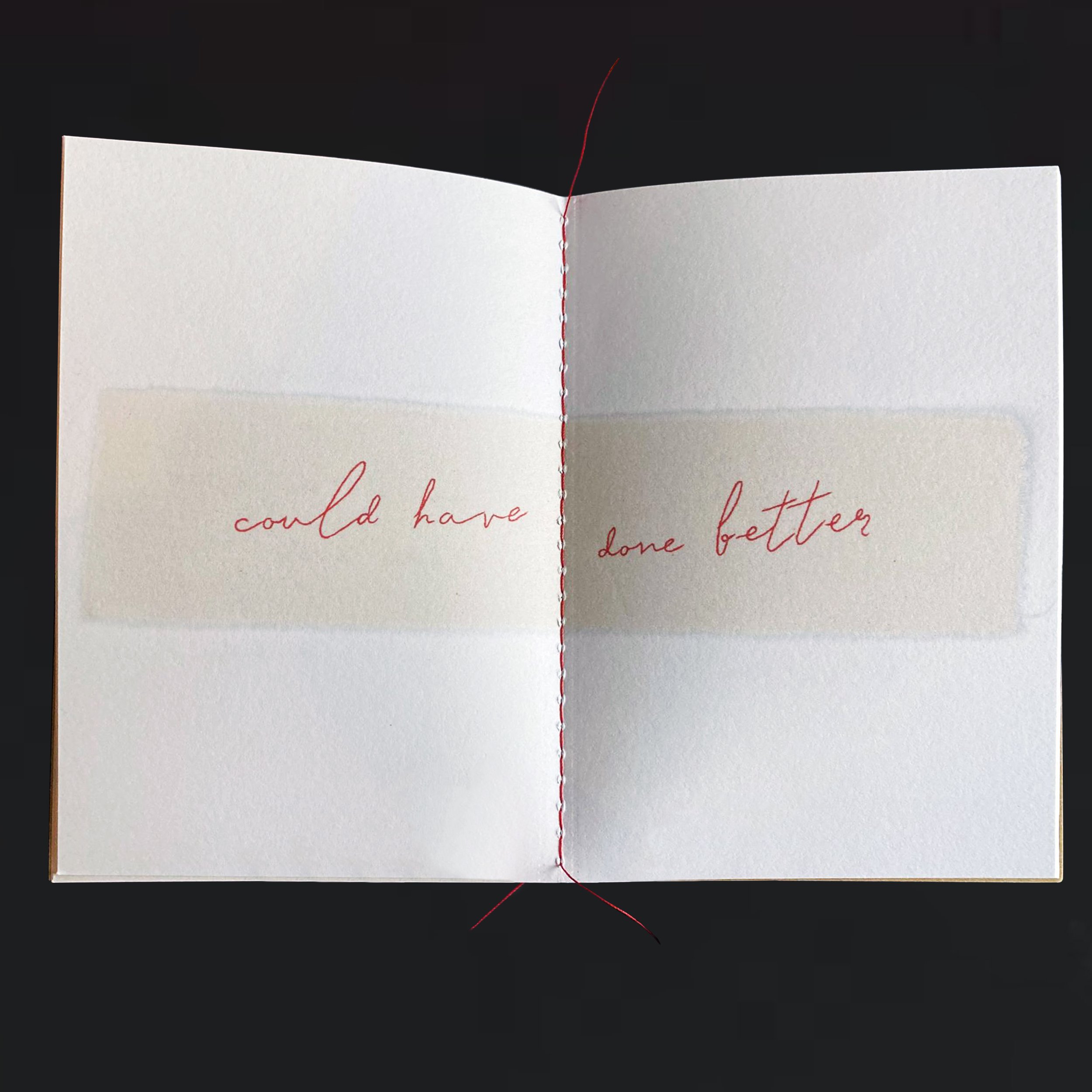 An open white book with red cursive writing on its pages, red and black thread stitched through the center, and a long red thread extending downward against a black background.