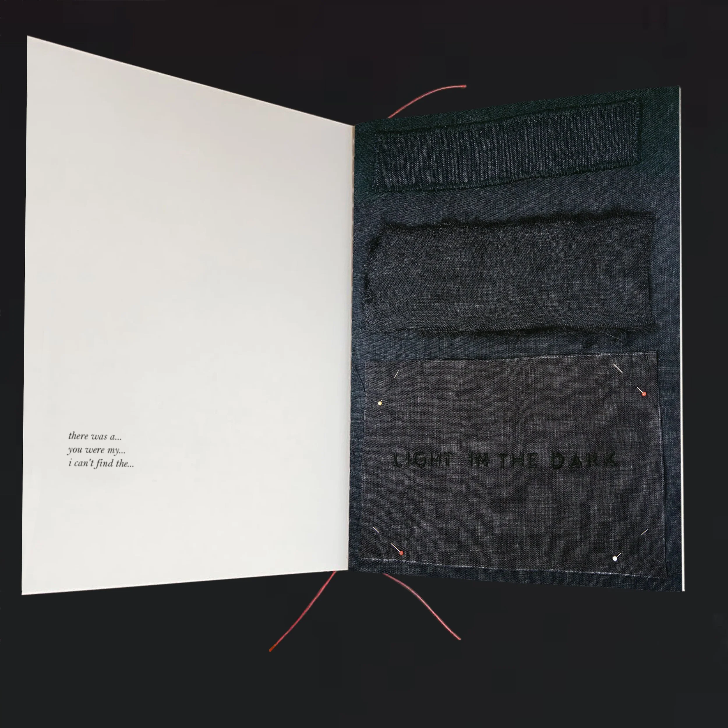Open book with dark fabric pockets on the right page and cursive text on the left page, with loose red and yellow thread on a black background.
