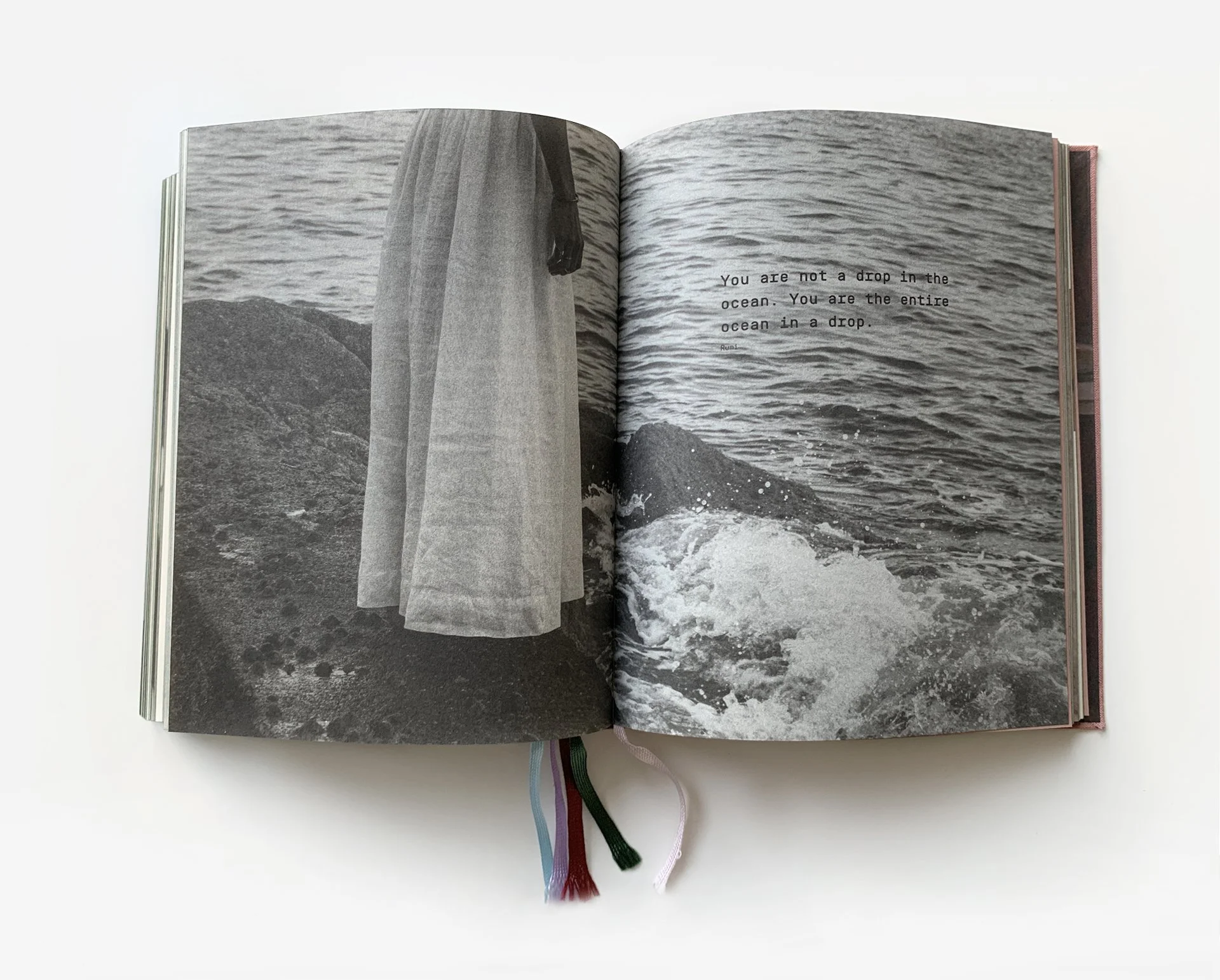 An open black and white photo book showing a person standing by the ocean with their arm hanging down, and a quote on the right page that reads, "You are not a drop in the ocean. You are the entire ocean in a drop."