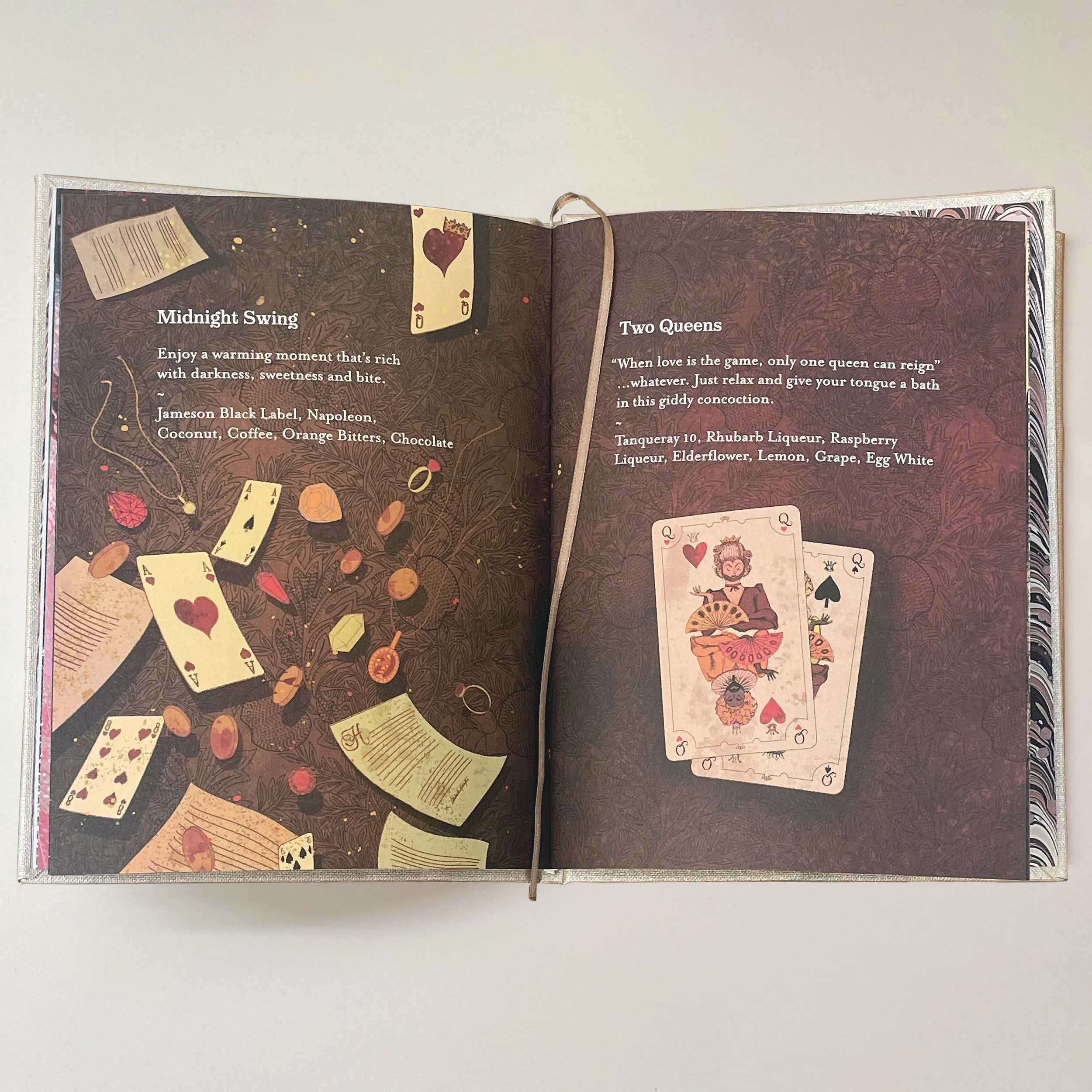 Open book showing pages with illustrations of playing cards, words, and card-related designs on a white background.