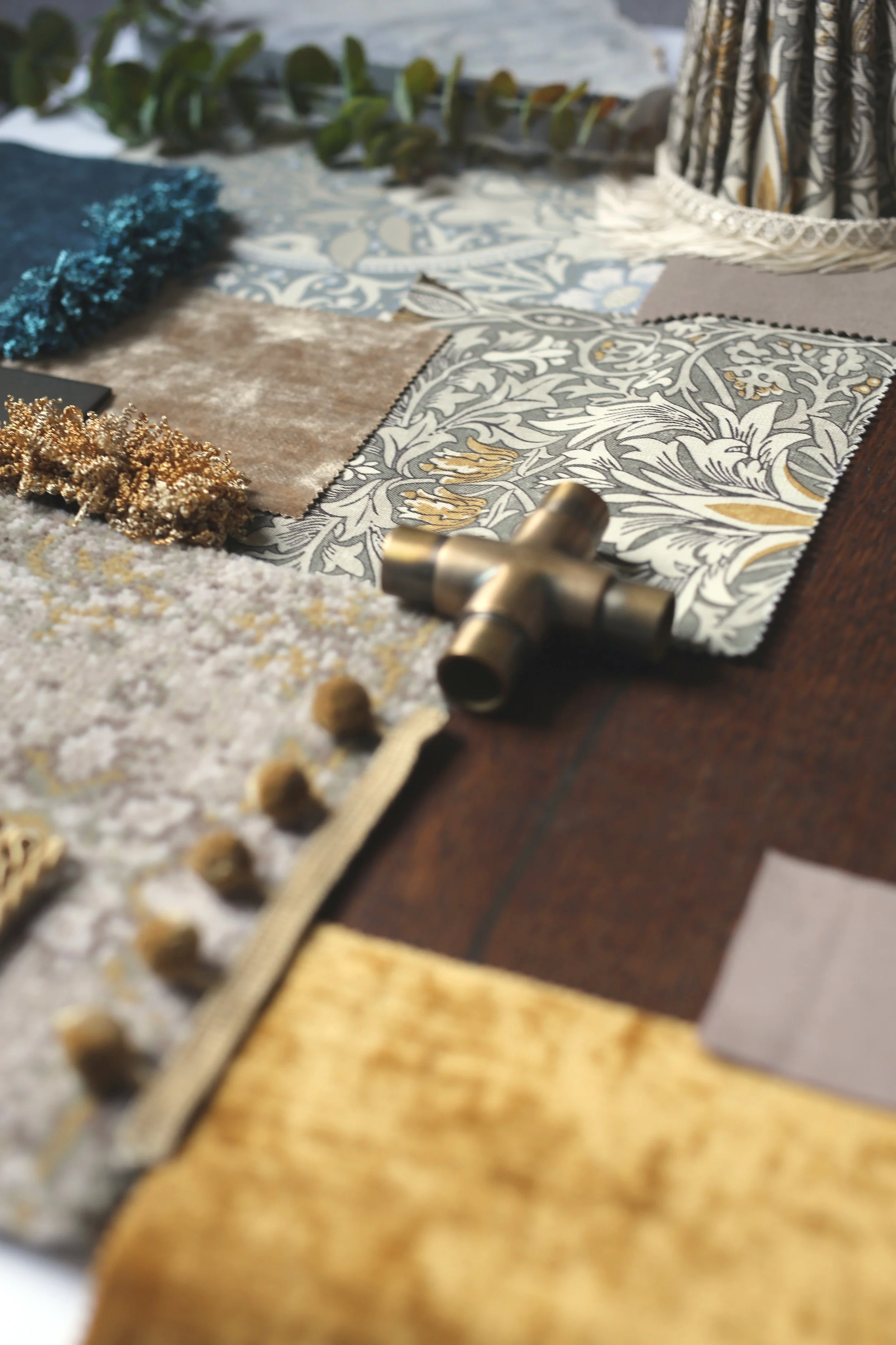 Close-up of fabric swatches and design samples on a table, with textured fabrics, printed textiles, and decorative items, for interior design planning.