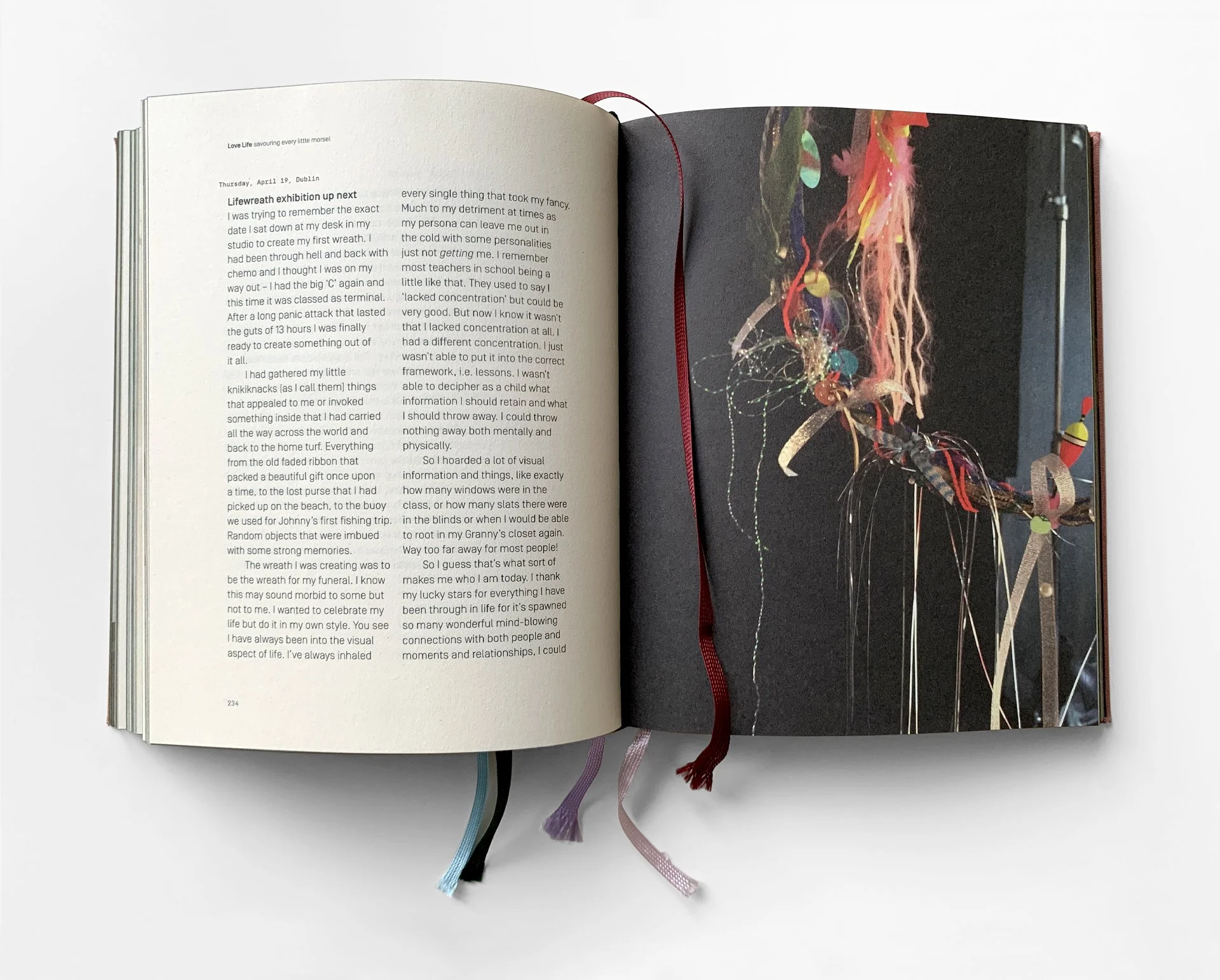 Open book lying on a white surface with ribbons sticking out, displaying pages with text on the left and a colorful abstract art on the right.