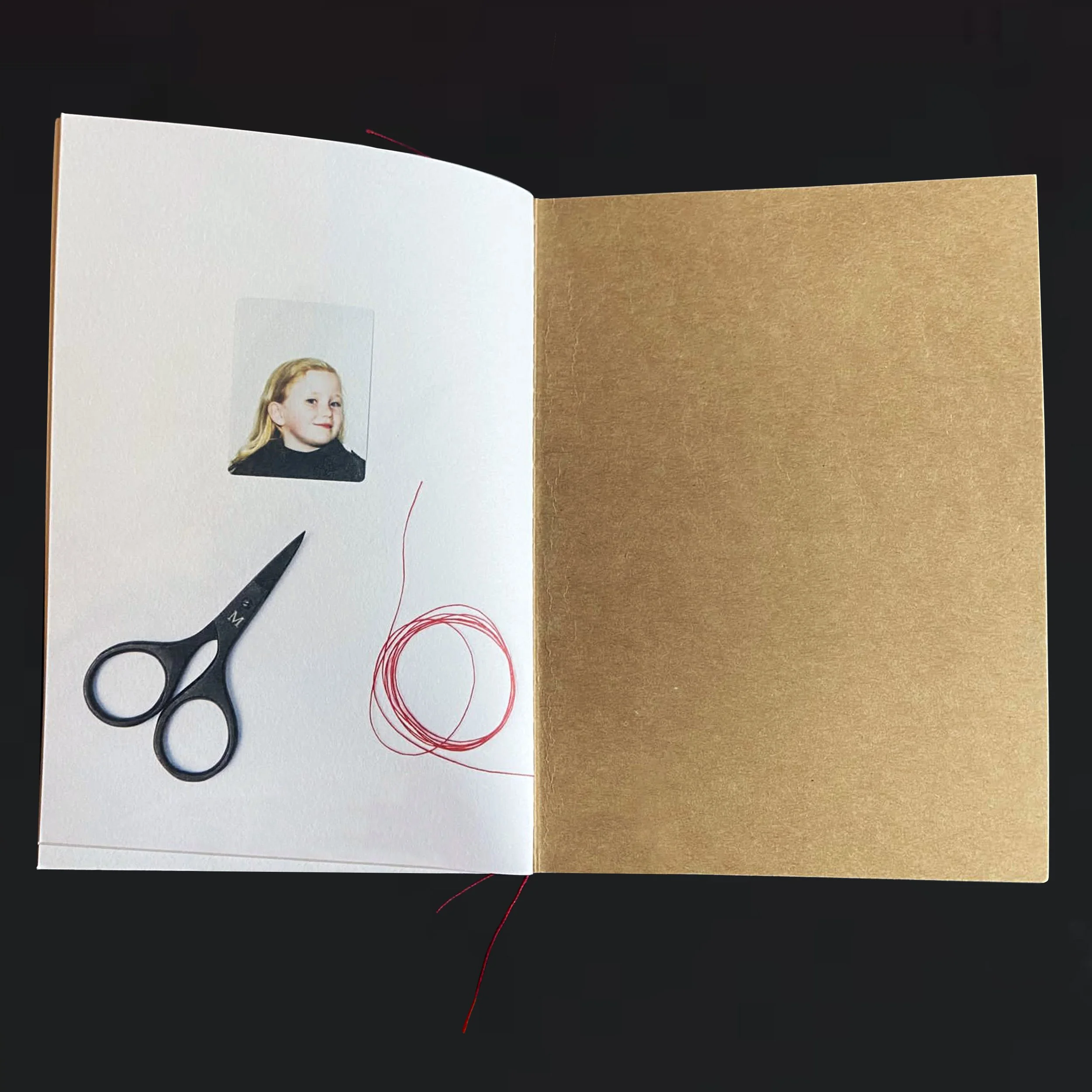 Open book with a photograph of a young girl on the left page, a pair of black scissors on the page next to her, and red thread on the right page against a black background.