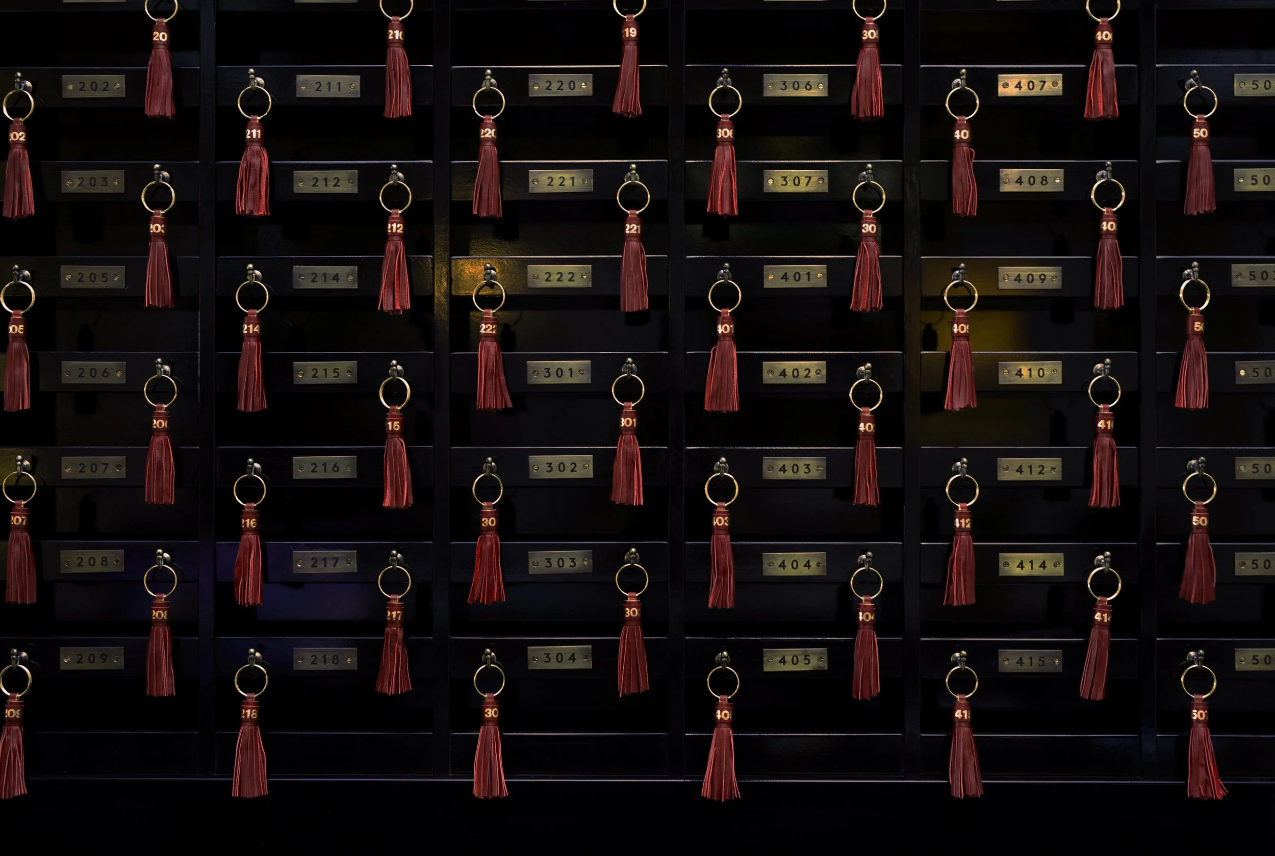 Wall of black lockers with gold nameplates and red leather keychains hanging from each locker's handle.