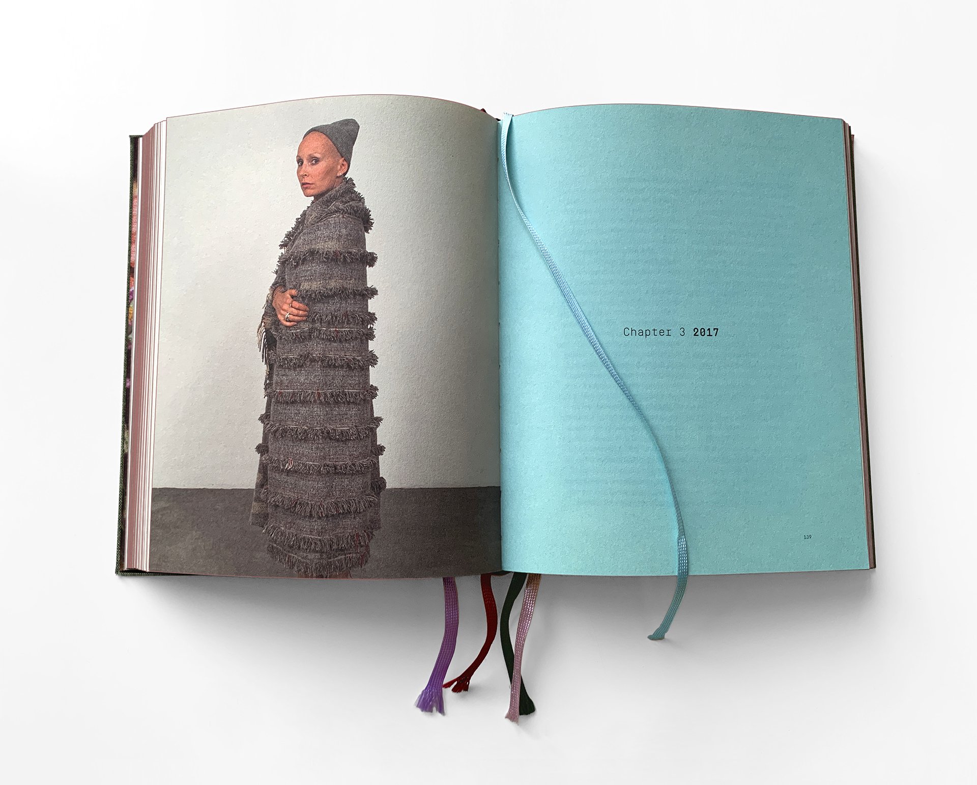 Open journal with a photograph of a woman in a gray beanie and textured gray coat on the left page and a blue chapter divider labeled "Chapter 3 2017" on the right page, with colored ribbons attached to the bottom.