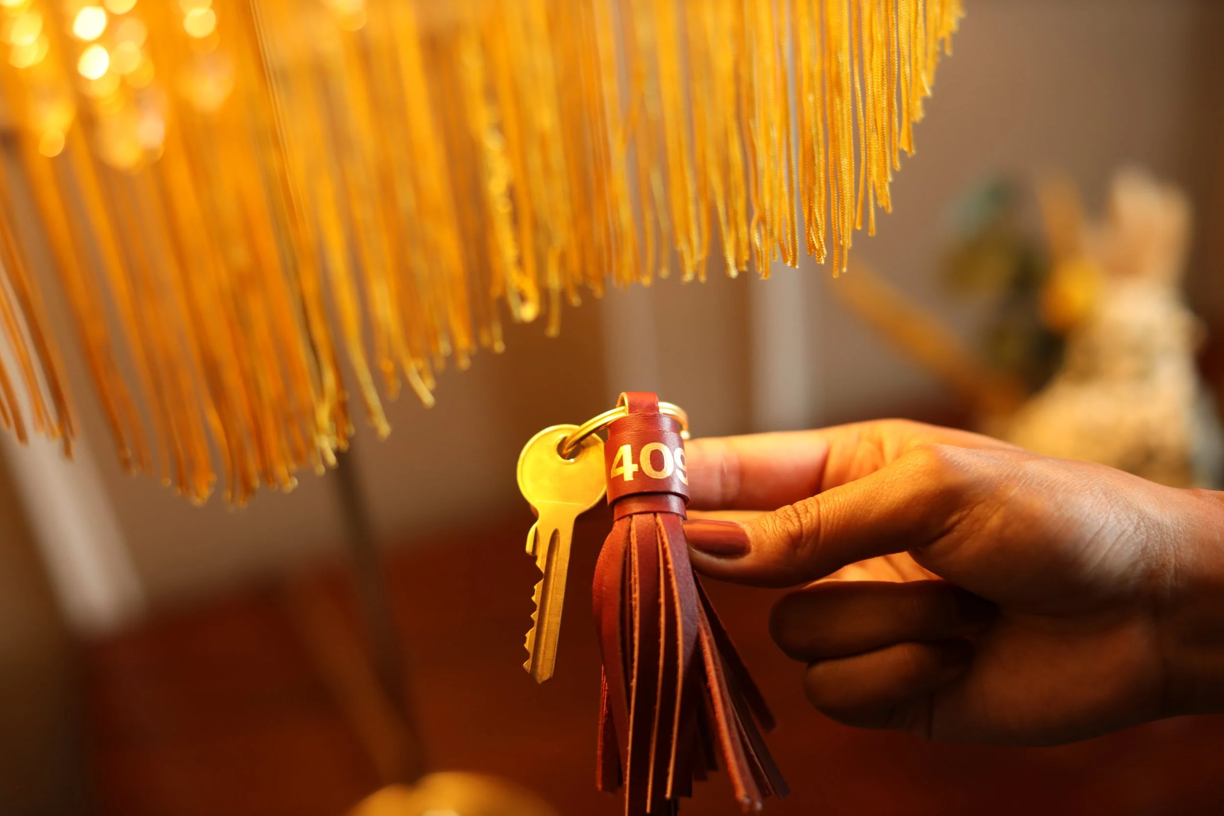 Close-up of a hand holding a brown leather bracelet with a yellow tag labeled '40s', in front of a display of yellow pasta hanging from above.