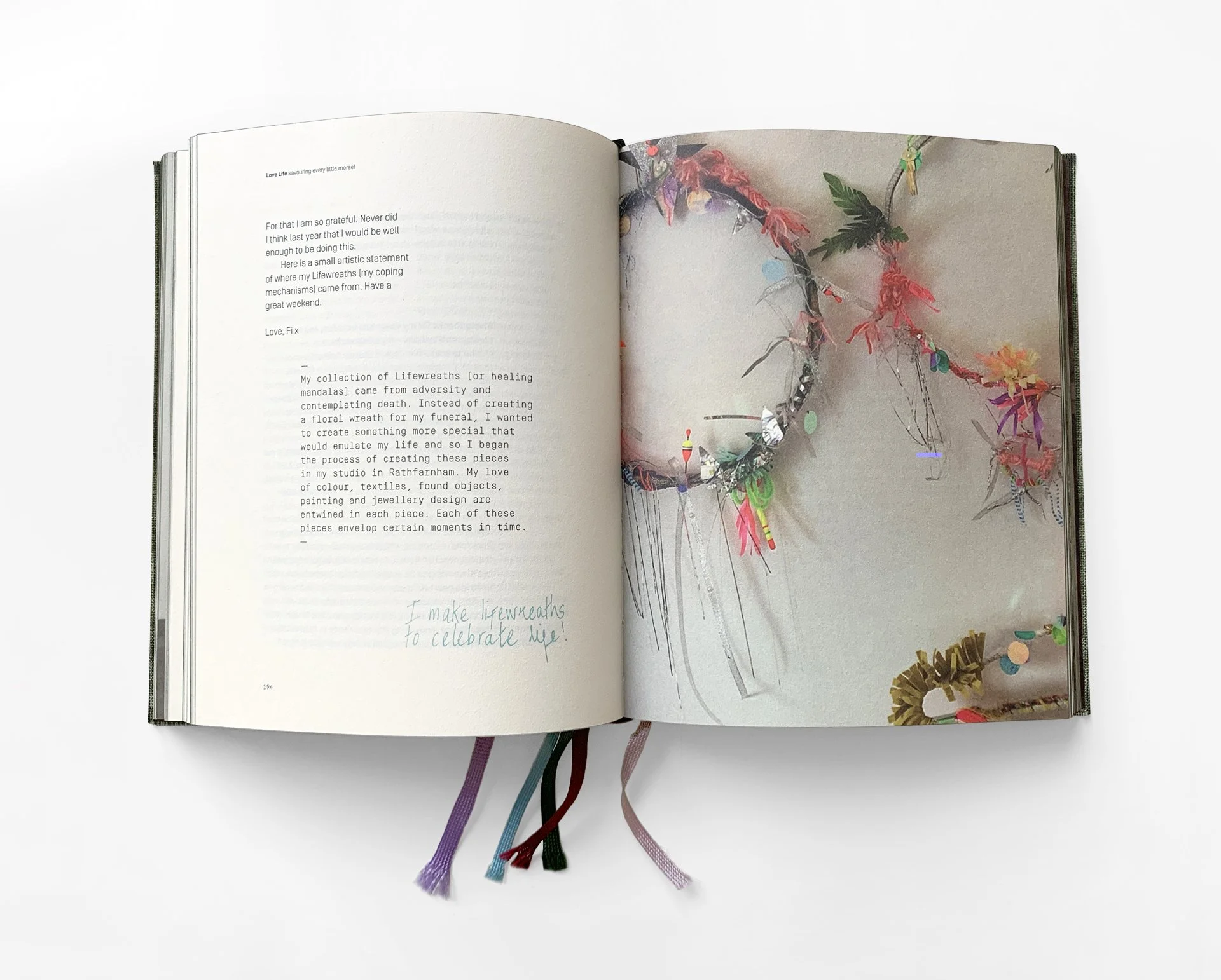 Open journal with handwritten notes and colorful paper craft decorations on the right page, and white space with text on the left page, lying on a white background.