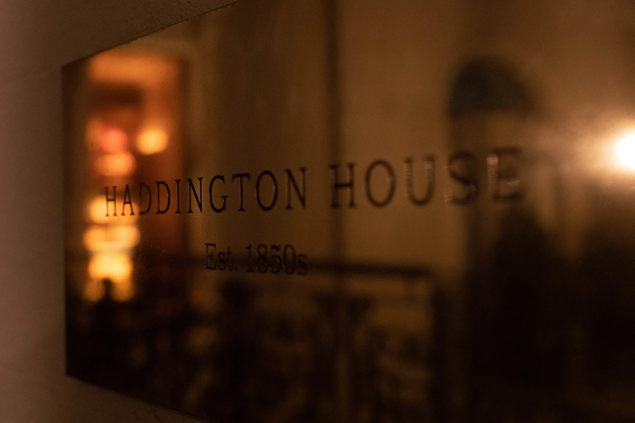 Close-up of a metallic plaque engraved with the words "Haddington House" and an establishment year of 1850, reflecting warm light.