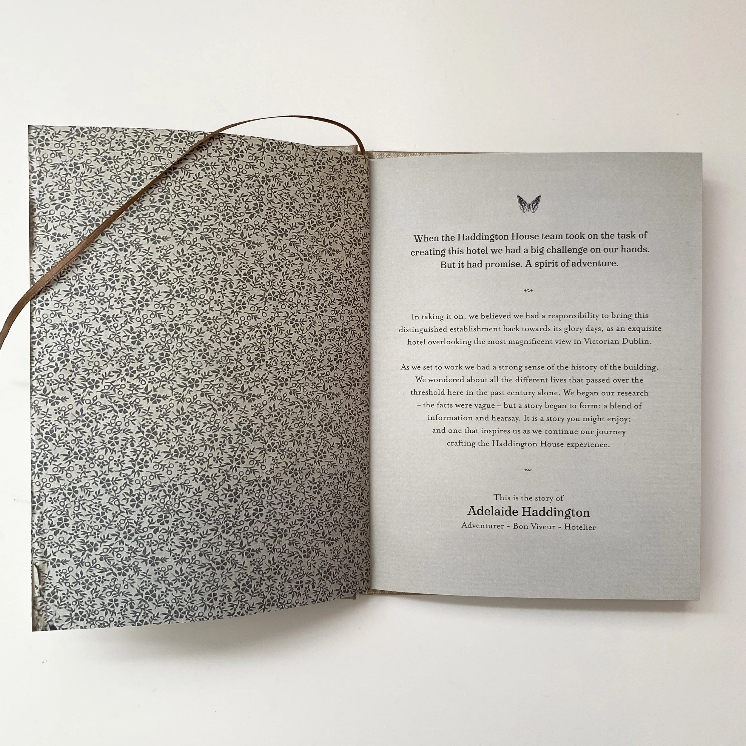 Open book showing a page with printed text and a butterfly illustration, partially covered by a patterned page from another book or magazine with small black floral motifs on white background.