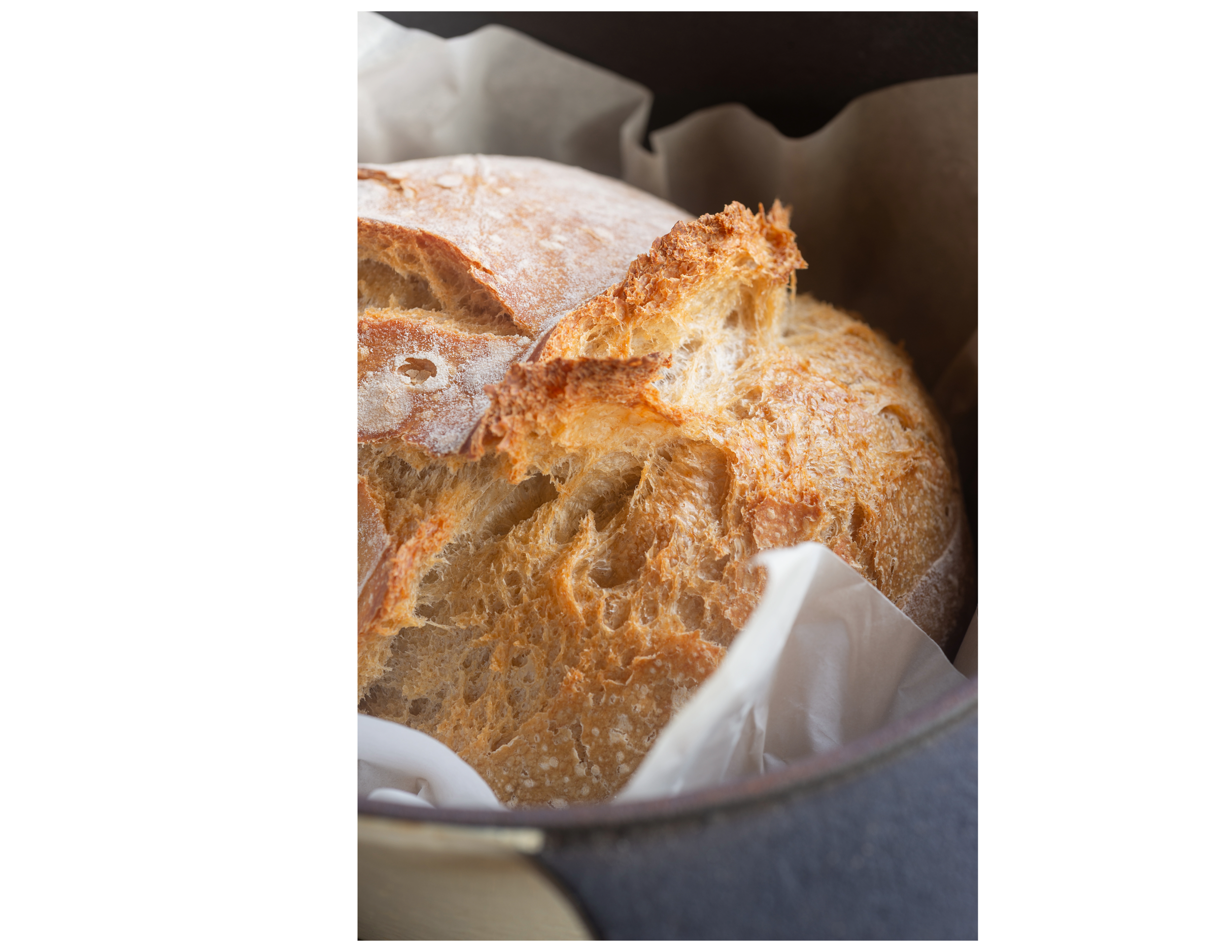 Close-up of a loaf of crusty sourdough bread placed inside a paper-lined basket.